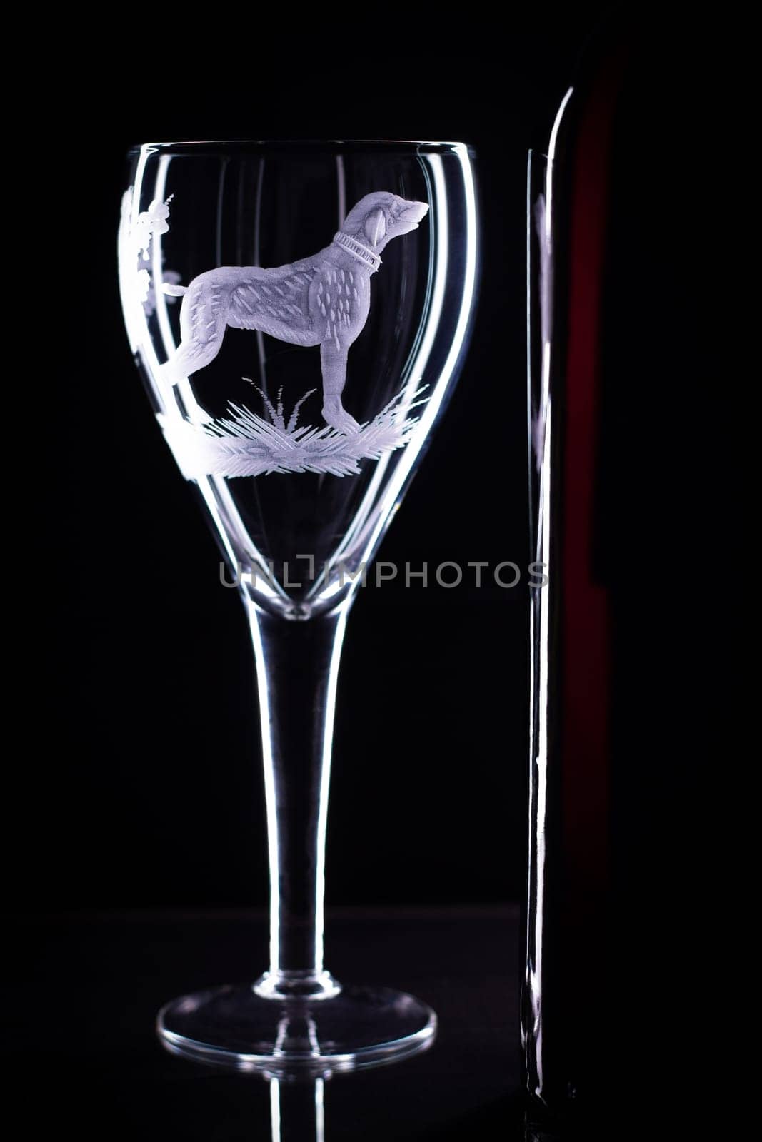 Wine glass with a sandblasted dog and a bottle of wine on a black background, copy space