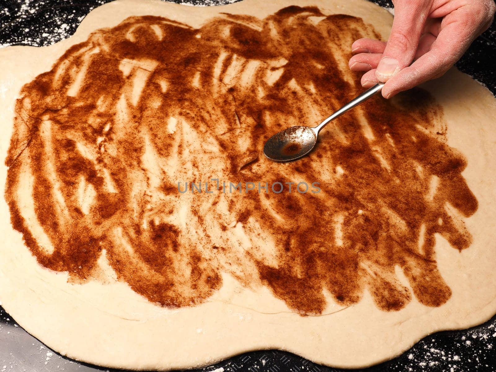 Baker or cook spreads rolled out organic yeast dough with cinnamon-sugar mixture, traditional handwork in the kitchen