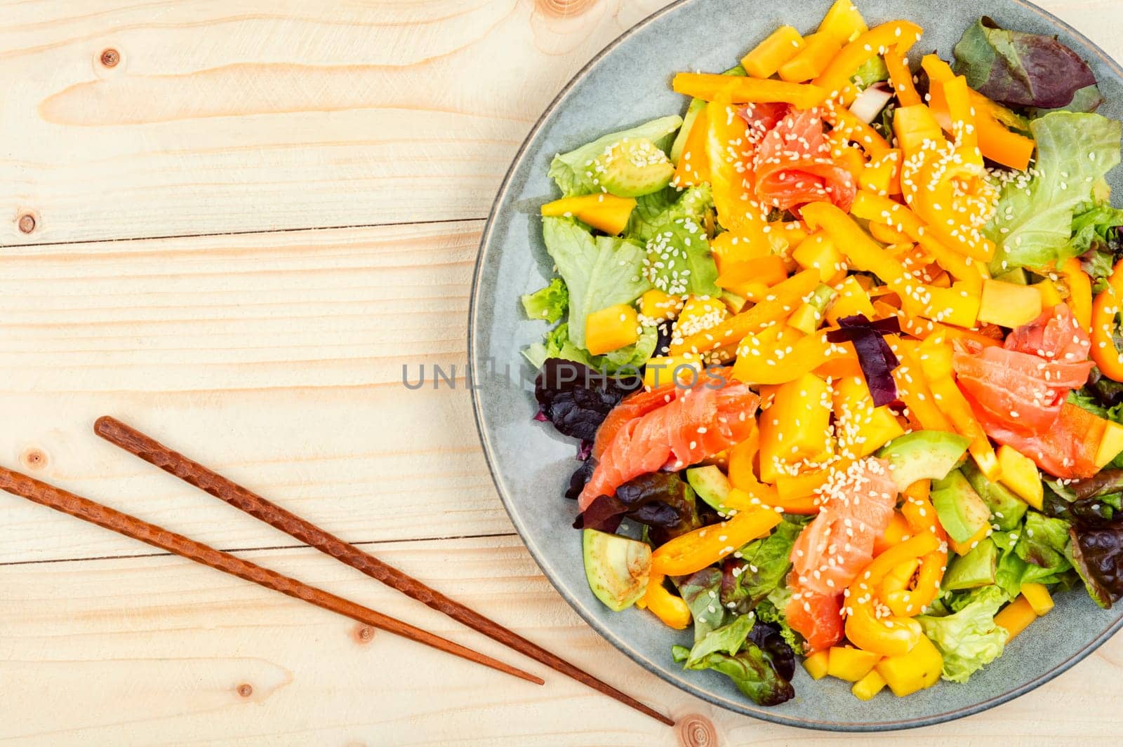 Tasty salad with salmon, mango, sesame avocado and pepper. Healthy eating, space for text. Food and chopsticks