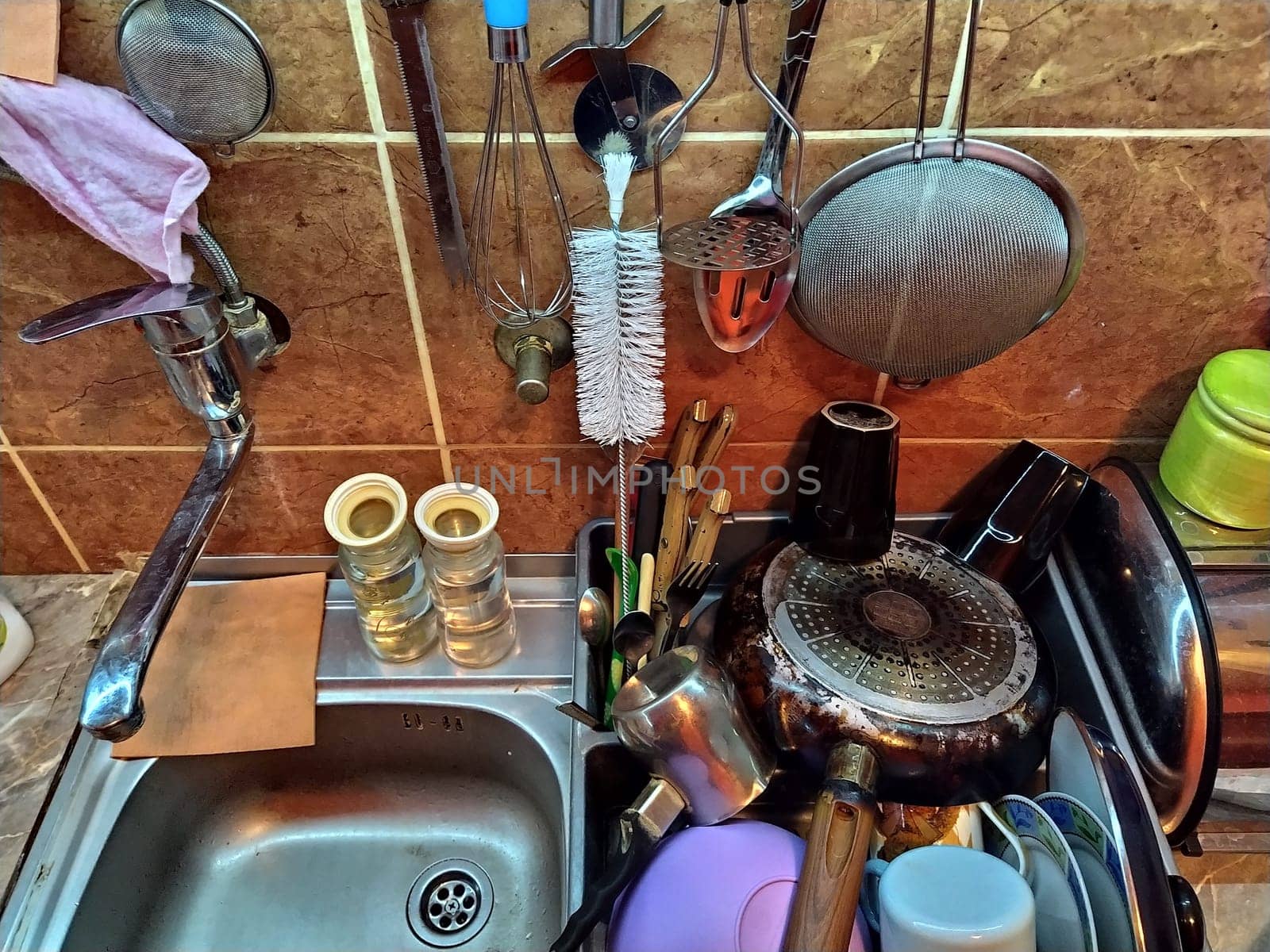 Belgrade, Serbia, December 12, 2020 Kitchen, countertop with sink, top view. Home daily life. The washed dishes are stacked near the sink. Kitchenware is hung on the tile wall. Colander, sponges rags.