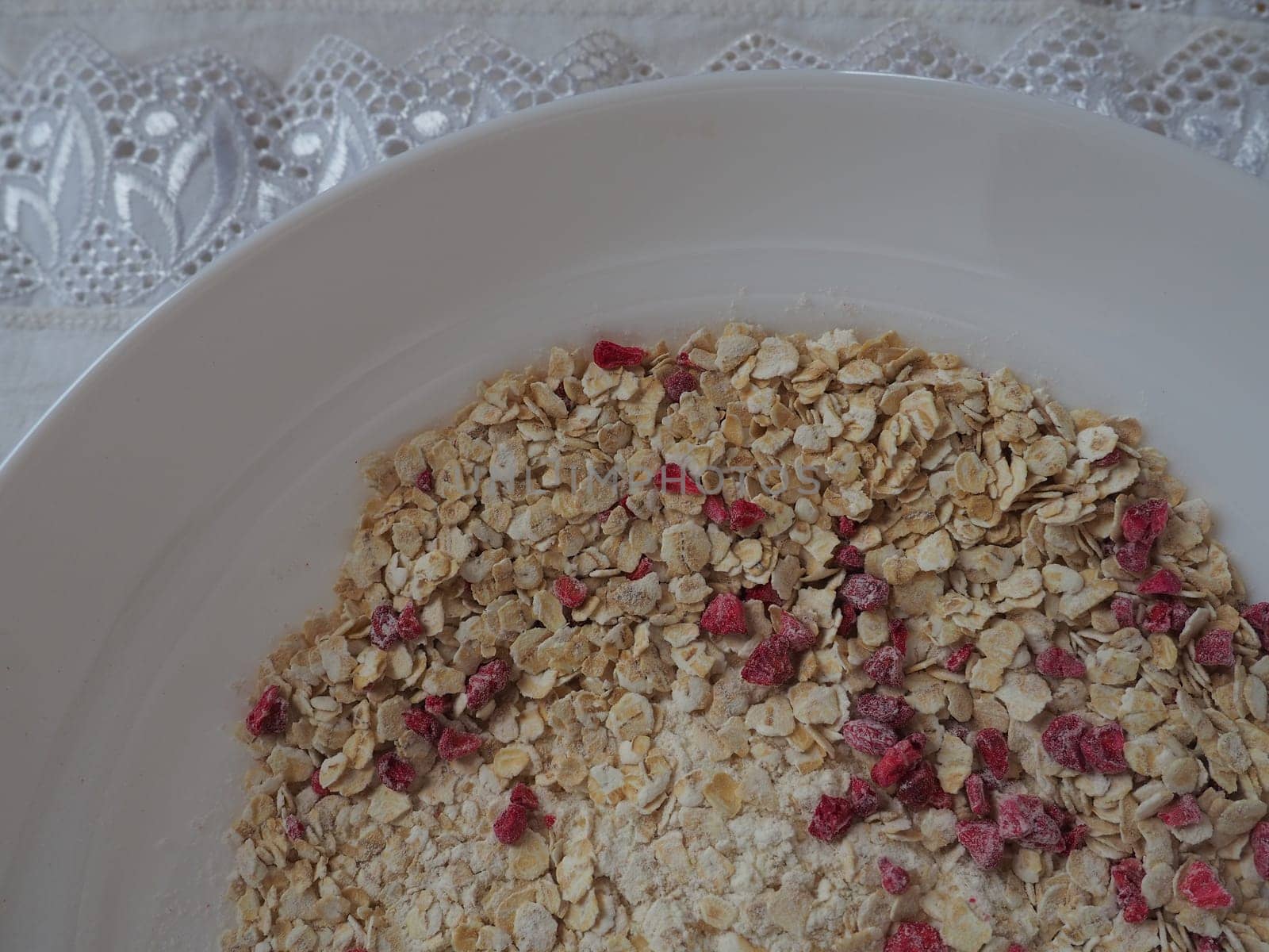 Organic Granola Cereal with oats, powdered sugar and dry raspberries. Healthy muesli as a dry mix. An antidiabetic, low calorie, healthy diet. White utensils.