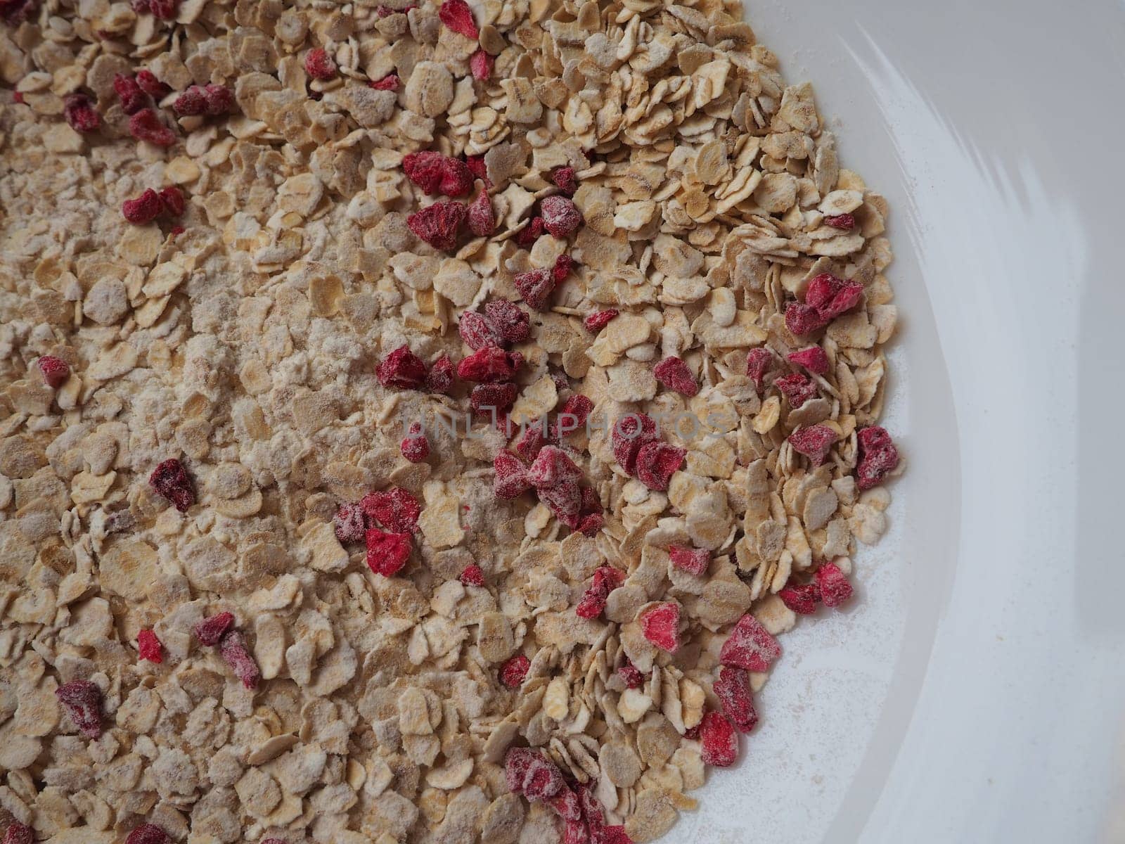 Organic Granola Cereal with oats, powdered sugar and dry raspberries. Healthy muesli as a dry mix. An antidiabetic, low calorie, healthy diet. White utensils.
