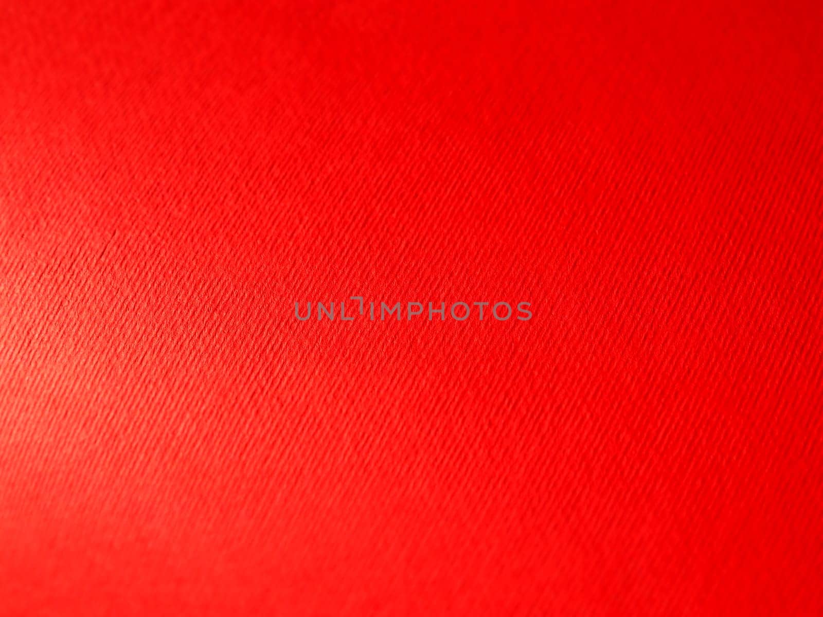 Abstract red background with texture. Close-up of paper surface with light and color gradient. Side lighting. Bright crimson backdrop.