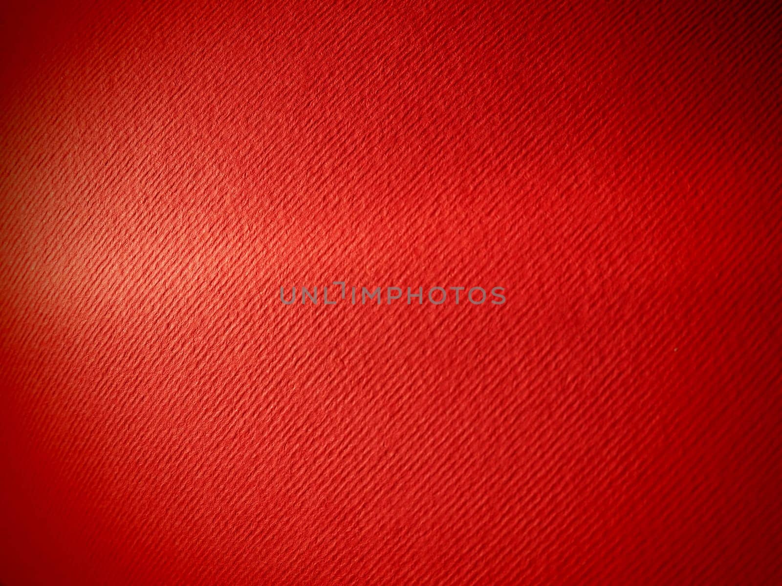 Abstract red background with texture. Close-up of paper surface with light and color gradient. Side lighting. Bright crimson backdrop.