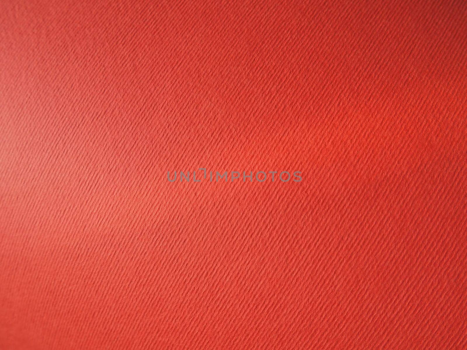 Abstract red background with texture. Close-up of paper surface with light and color gradient. Side lighting. Bright crimson backdrop.