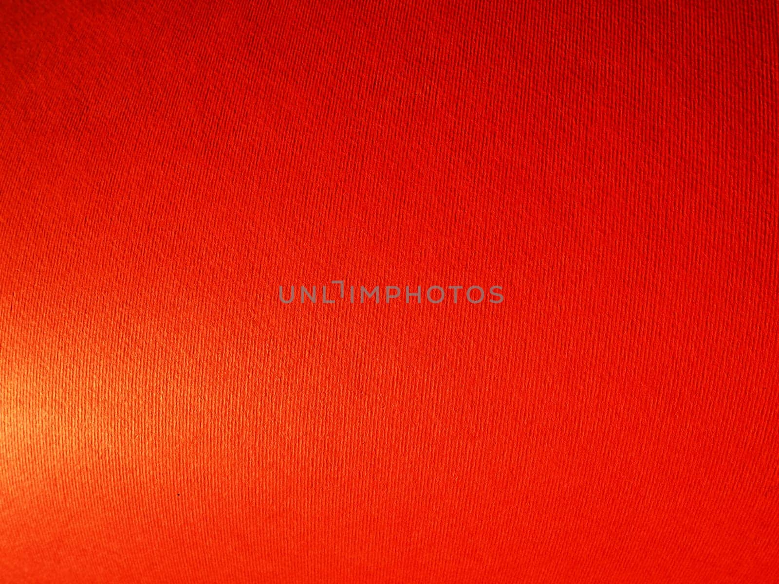 Abstract red background with texture. Close-up of paper surface with light and color gradient. Side lighting. Bright crimson backdrop.