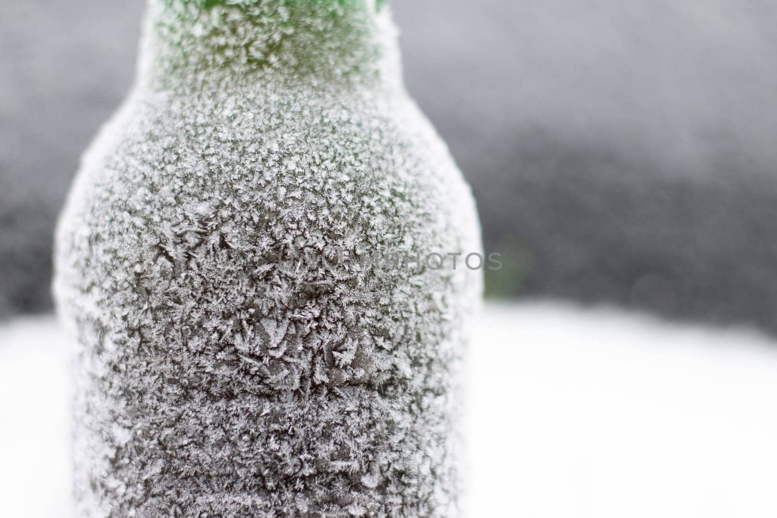 Partially blurred bottle of beer covered with hoarfrost in snow on dark background, copy space