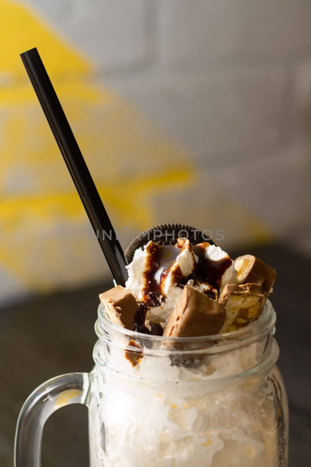 Freakshake in jar with cocktail straw, chunks of chocolate and cookies on dark wooden table. Vertical