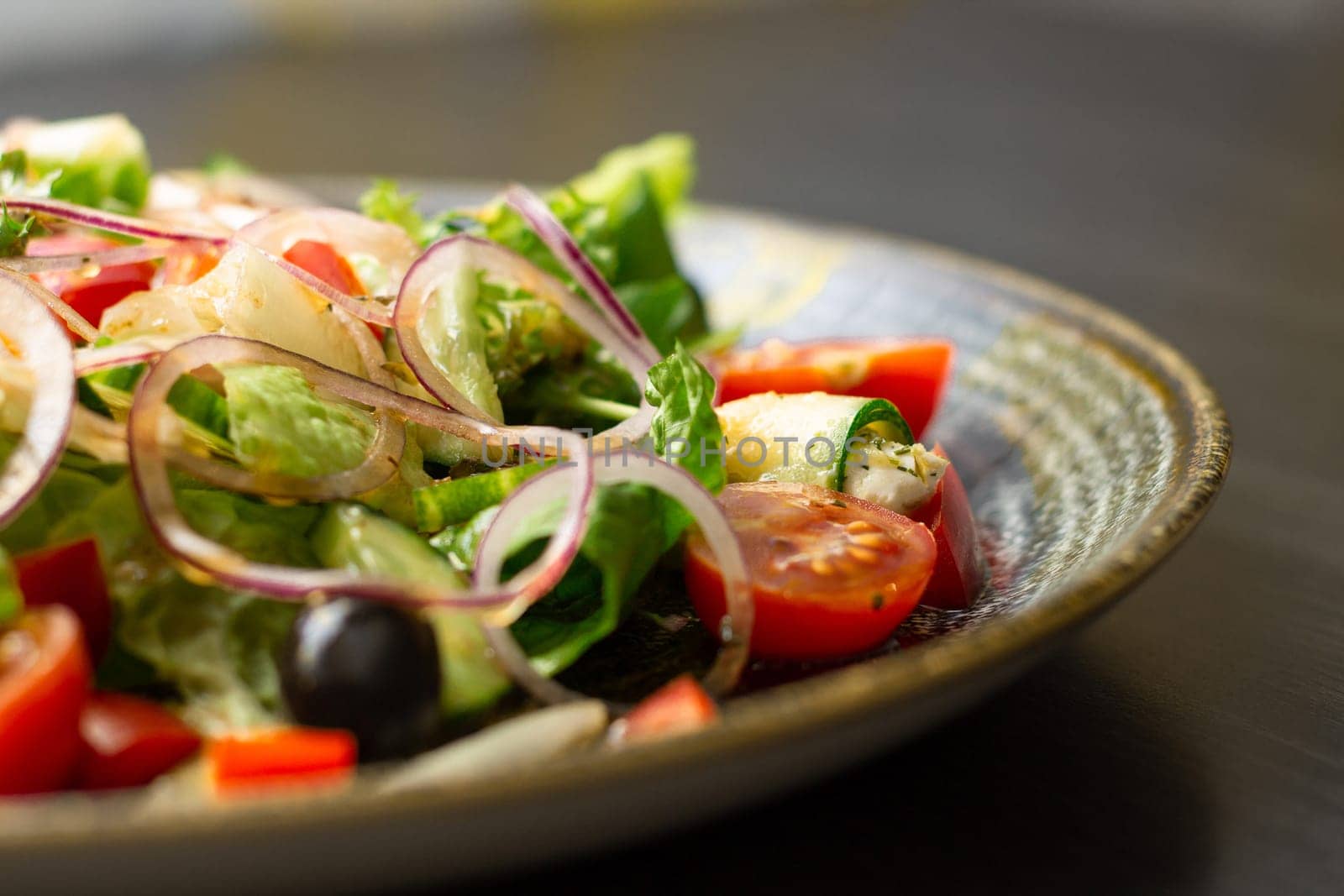 Vegetable salad with greens and olives in dark clay plate on wooden table