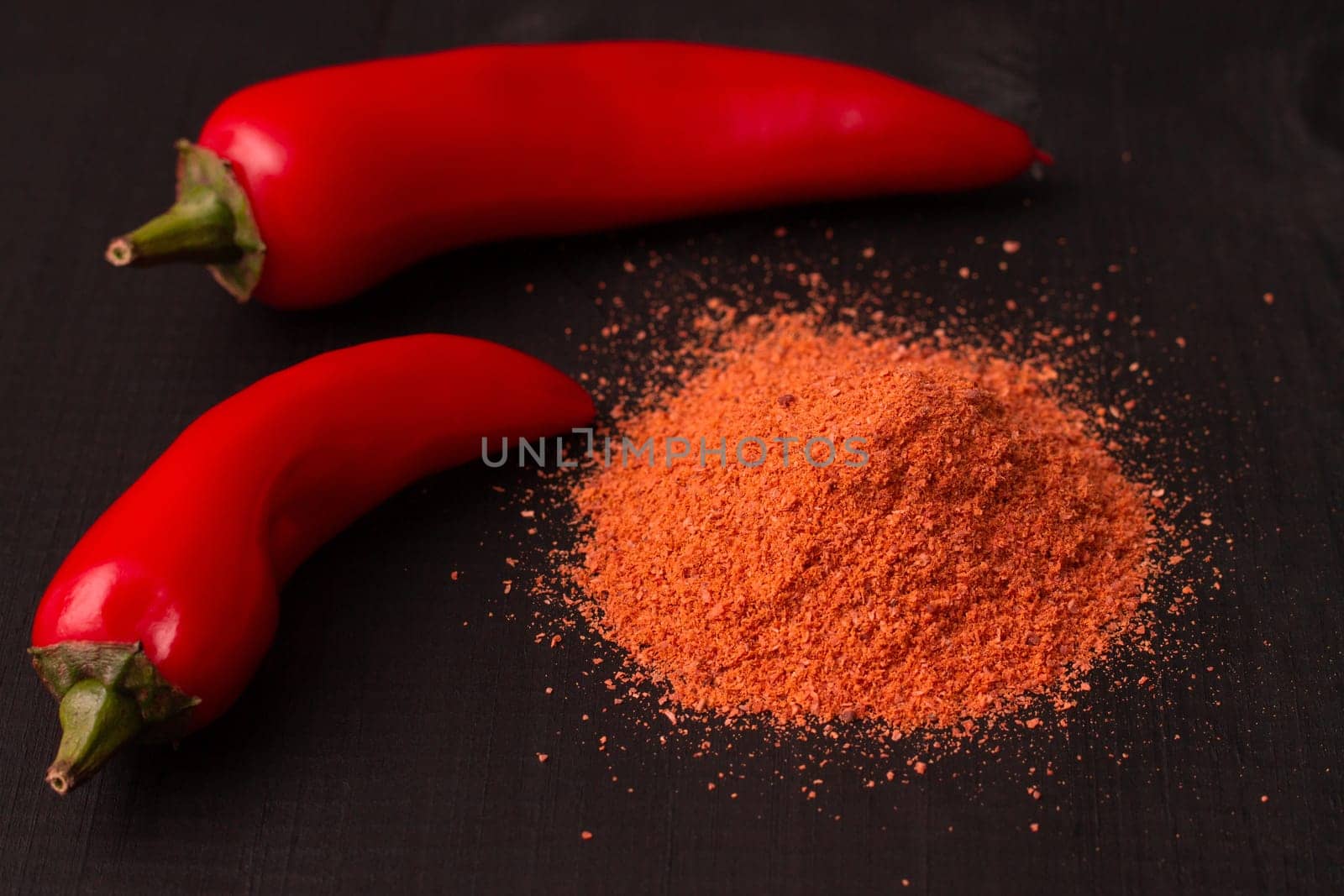 Two pods of red hot jalapeno peppers with a slide of pepper powder on a black wooden surface.