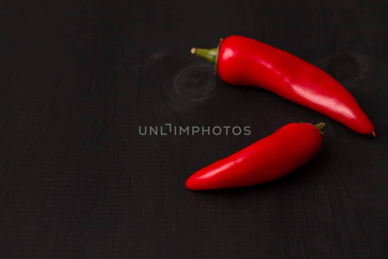 Two pods of red hot jalapeno peppers on a black wooden surface, copy space