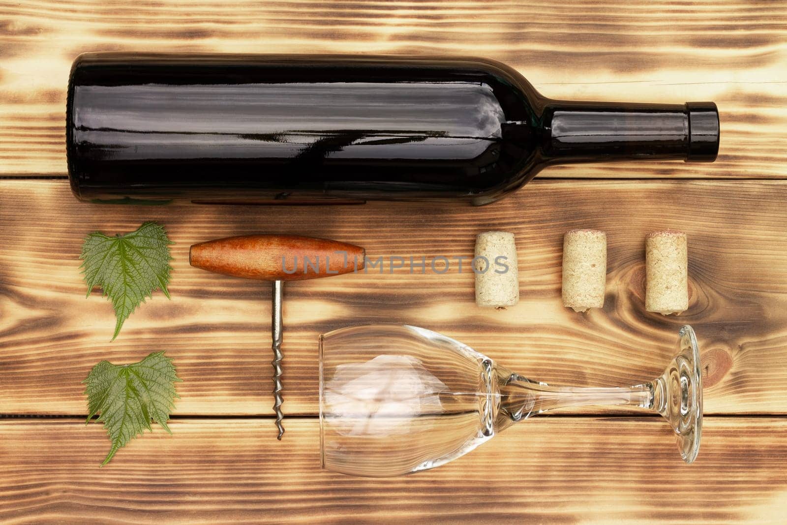 Wine glass, corkscrew, corks, wine bottles, grapevine on rustic burnt wooden background. Top view, copy space