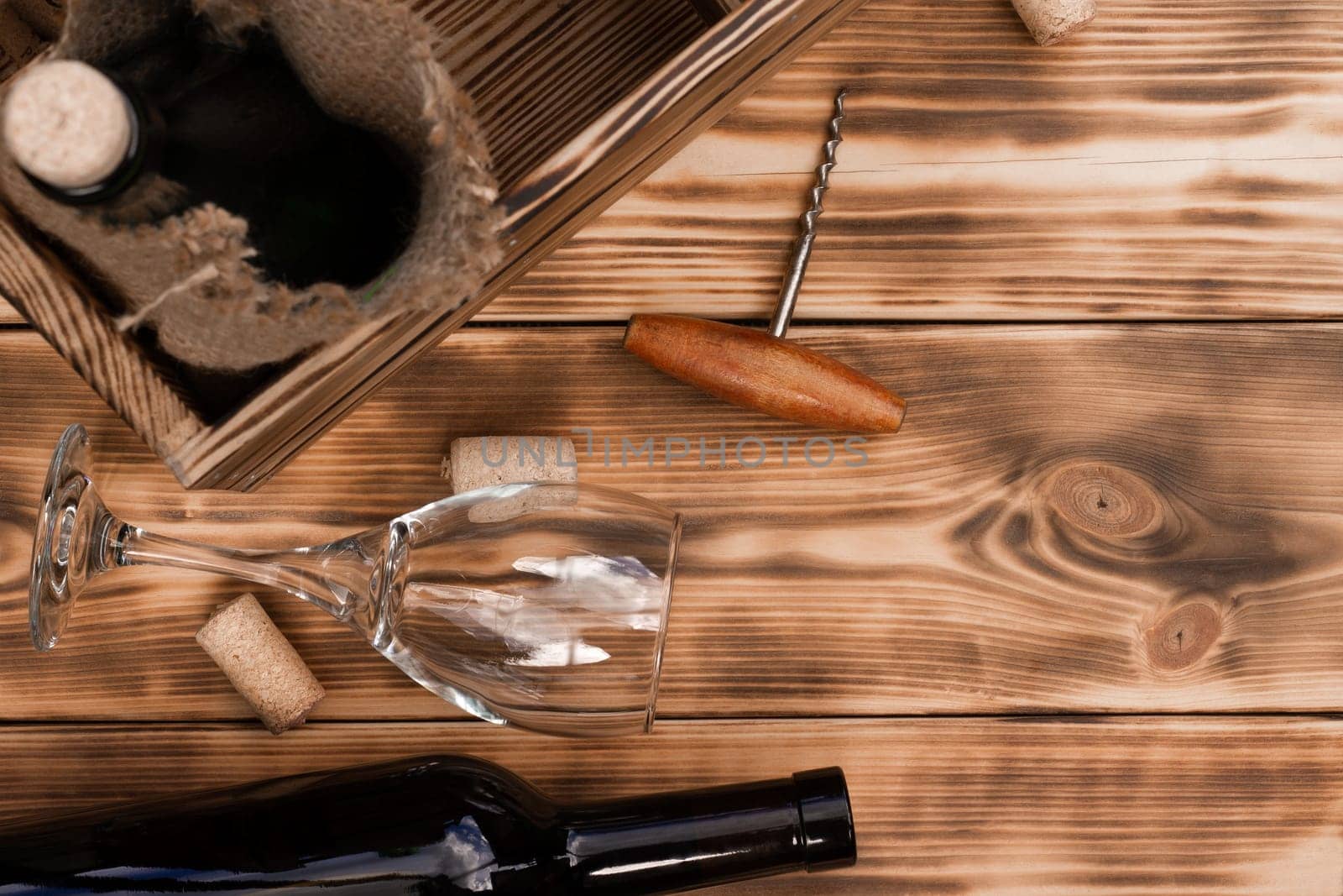 Wine glass, corkscrew, corks, wine bottles, grapevine on rustic burnt wooden background. Top view, copy space