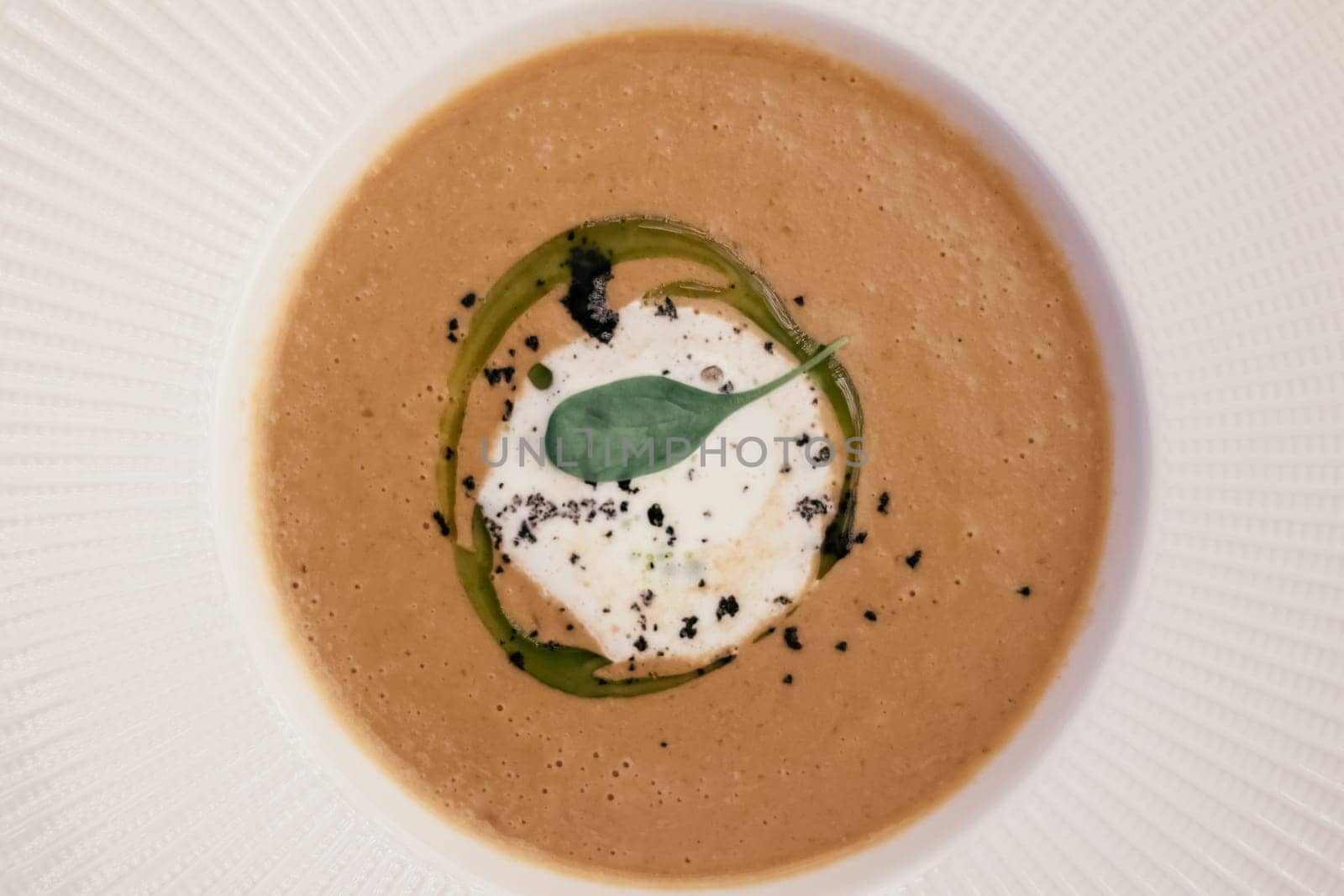 Tasty delicious thick brown pumpkin mushroom cream soup with mascarpone truffle pasta, herb sauce, green leaf in white circle mousse, condiment and seeds. White stripe plate background. Top view