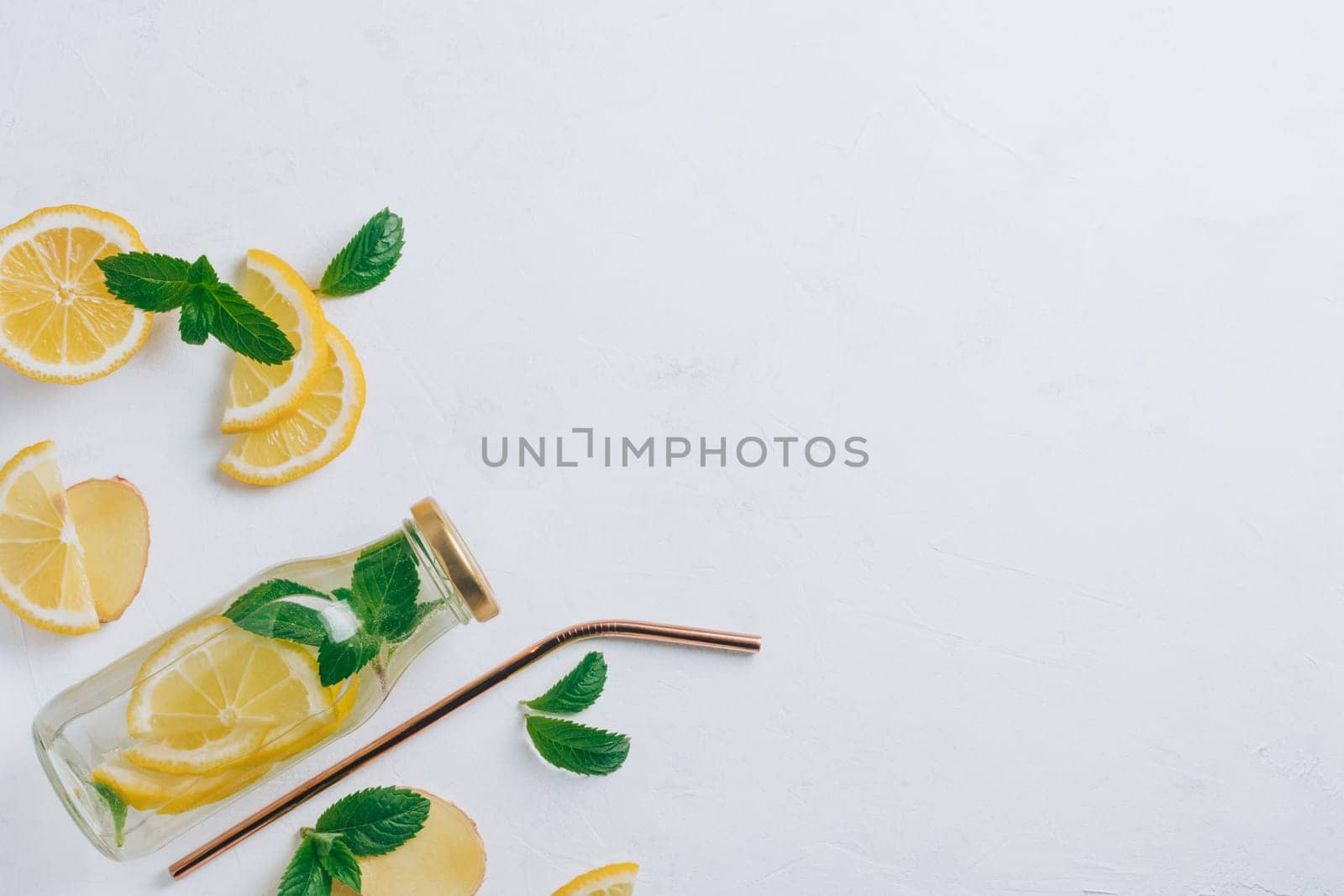 Glass bottle with lemonade with metal straw and ingredients for cooking. Ginger, lemon, mint on white surface. Flat lay, top view. Copy space