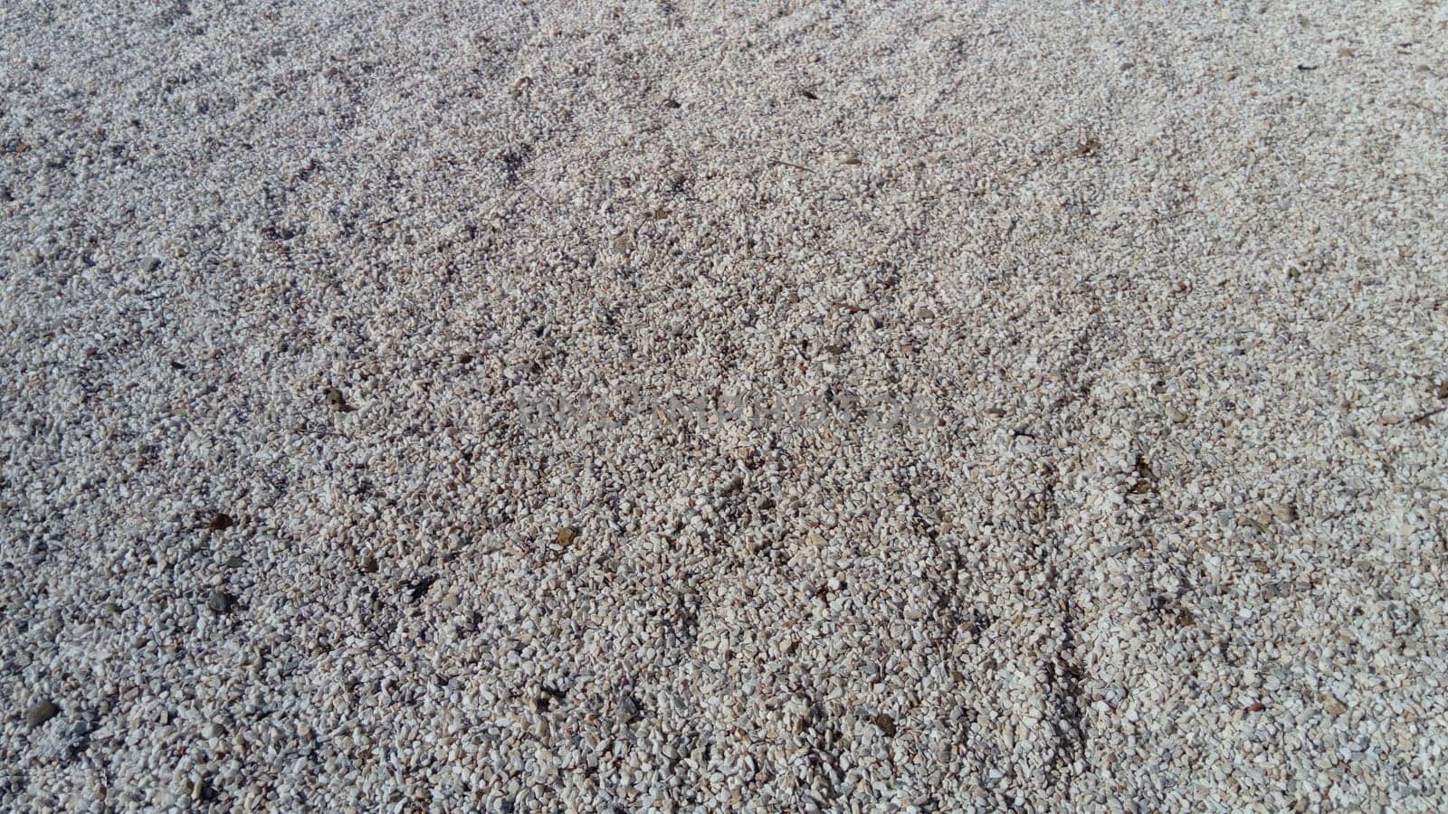 White small pebbles or decorative gravel. Natural daylight. The texture of the stone with a rough surface. Pebble beach.