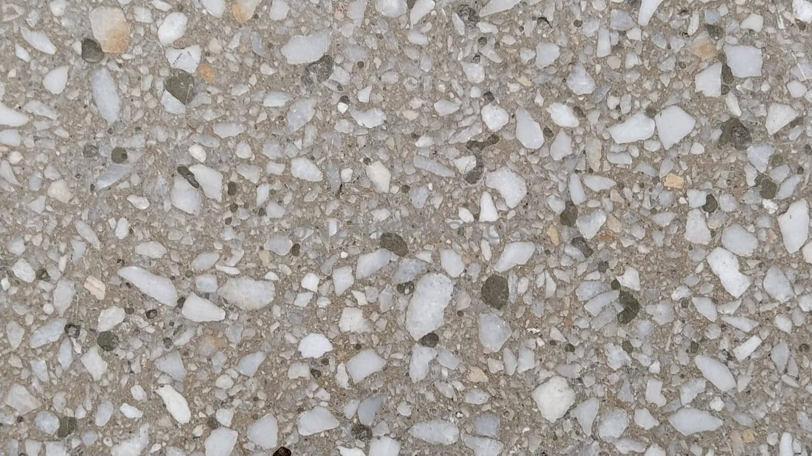 Concrete surface with multi-colored blotches of small stones. Light beige tone. Wall of a building or concrete slab. Close-up. Pockmarked cement surface. Interior or exterior finish option.