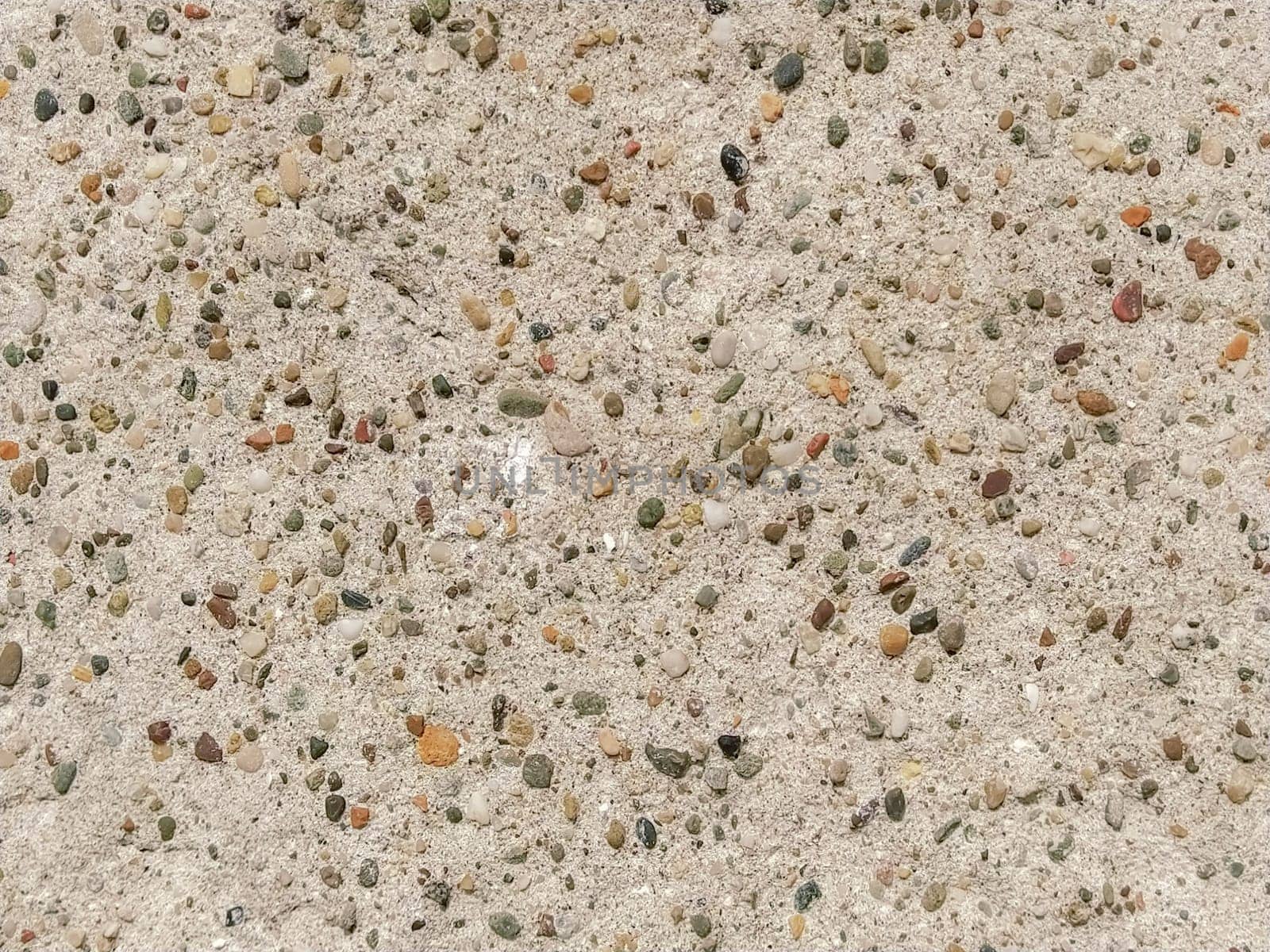 Concrete surface with multi-colored blotches of small stones. Light beige tone. Wall of a building or concrete slab. Close-up.