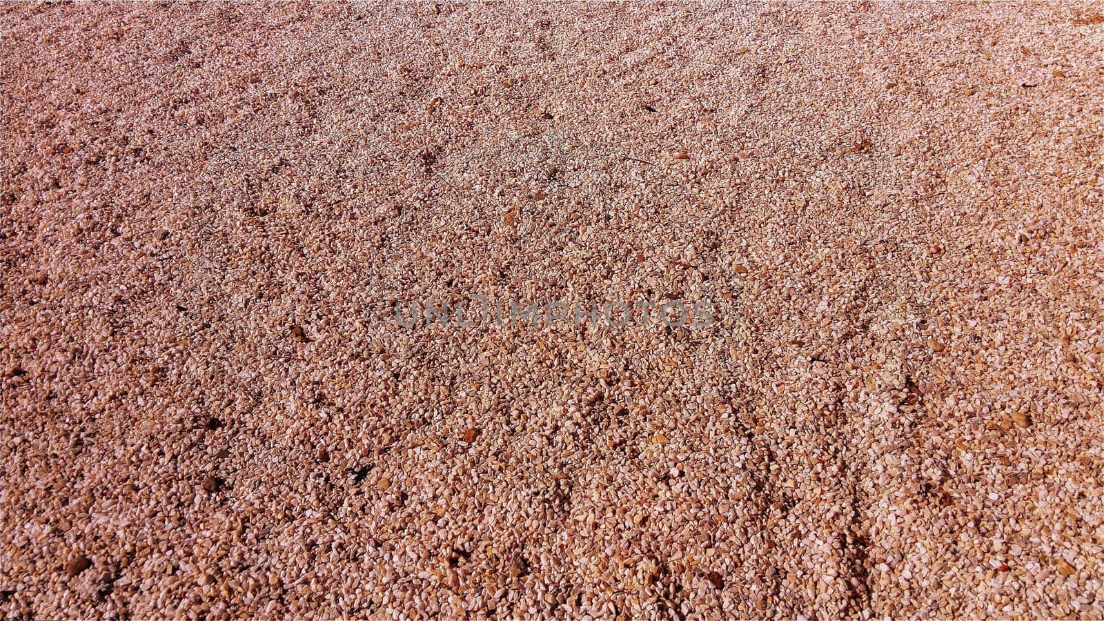 Red small pebbles or decorative gravel. Natural daylight. The texture of the stone with a rough surface. Pebble beach.