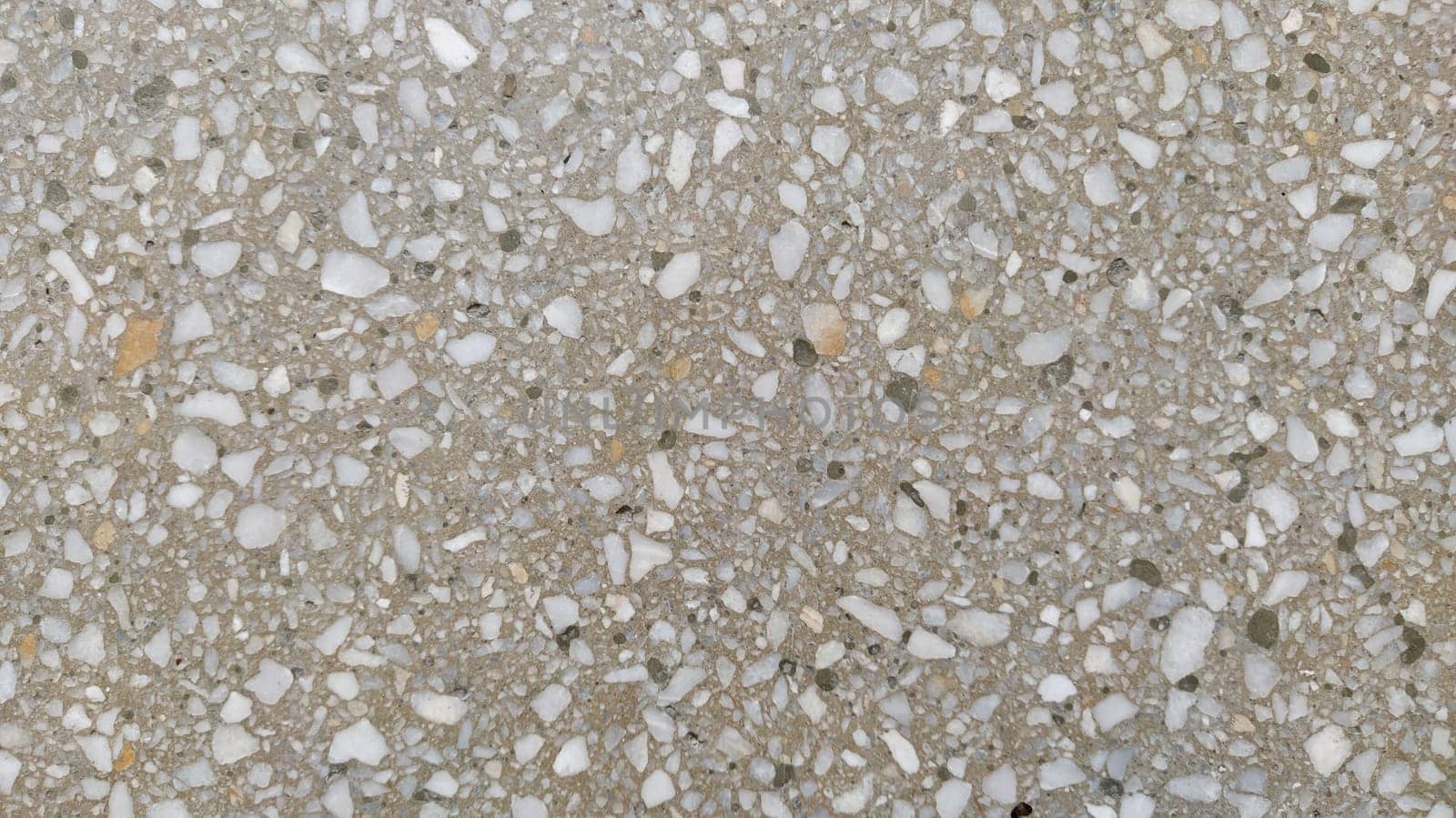 Concrete surface with multi-colored blotches of small stones. Light beige tone. Wall of a building or concrete slab. Close-up. Pockmarked cement surface. Interior or exterior finish option.