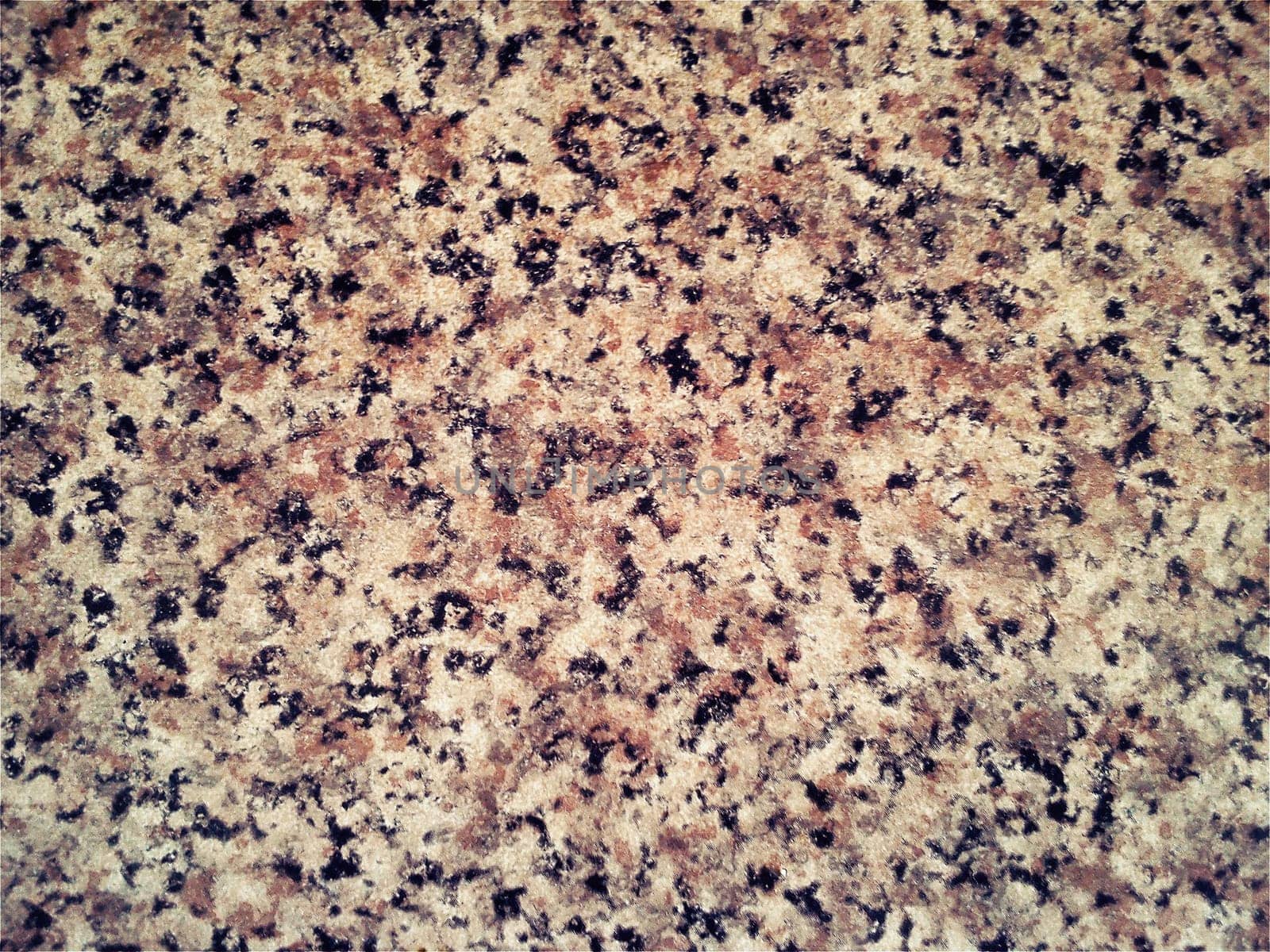 Granite smooth surface or slab in warm brown, gray, beige tones with frequent black spots and dots. Variant of interior decoration. Close-up. Natural background. Stone cut.