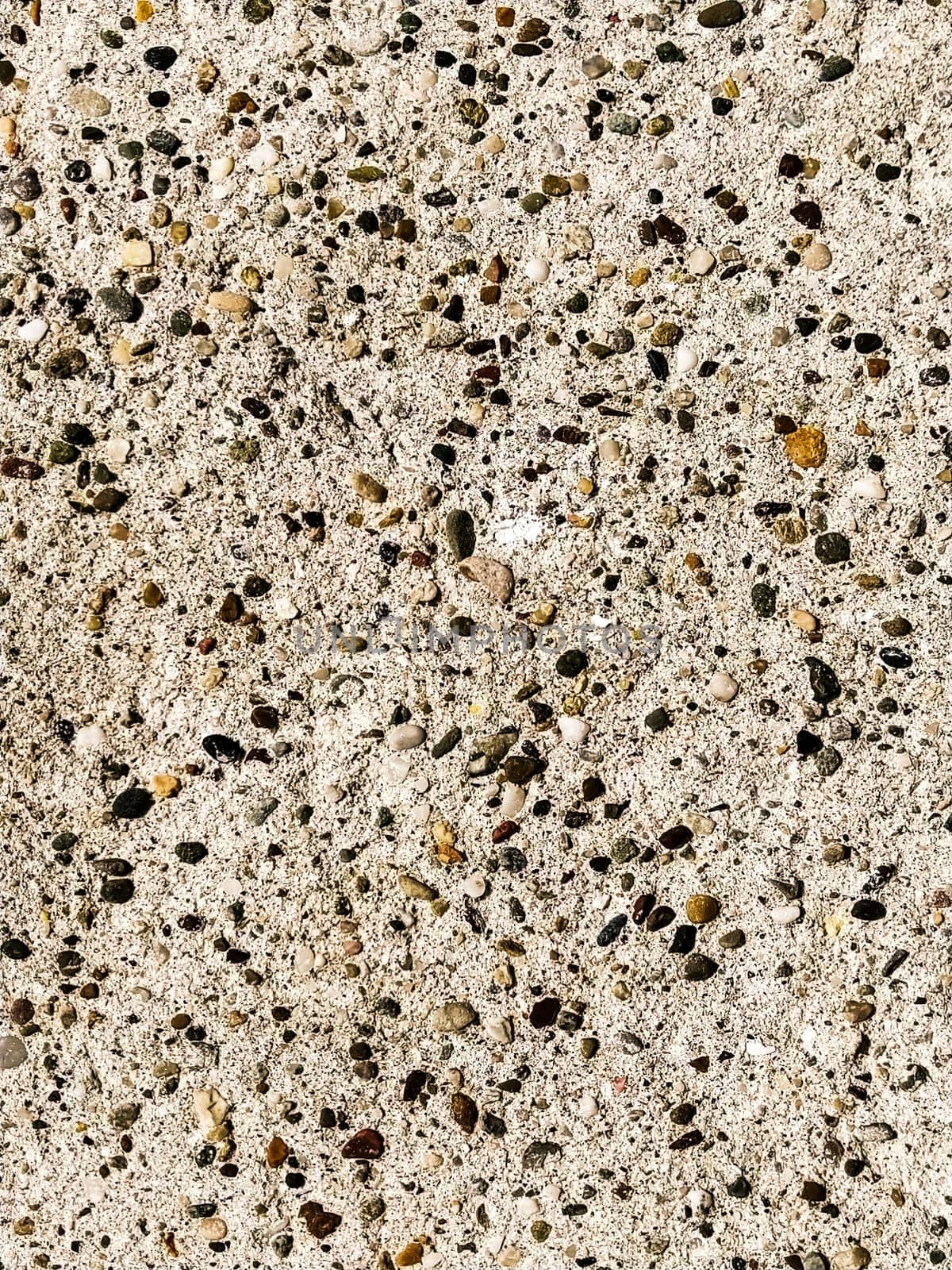 Concrete surface with multi-colored blotches of small stones. Light beige tone. Wall of a building or concrete slab. Close-up. Pockmarked cement surface. Interior or exterior finish option.