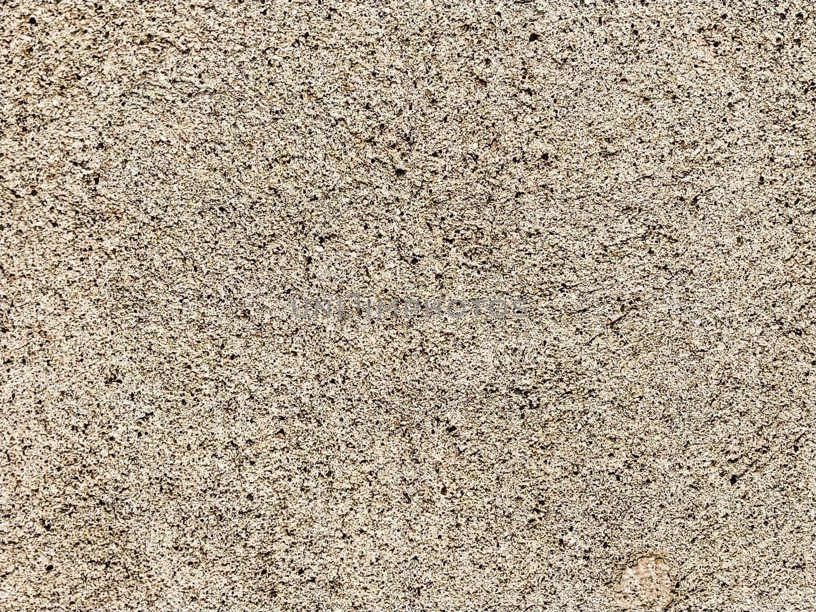 Concrete surface with multi-colored blotches of small stones. Light beige tone. Wall of a building or concrete slab. Close-up. Pockmarked cement surface. Interior or exterior finish option.