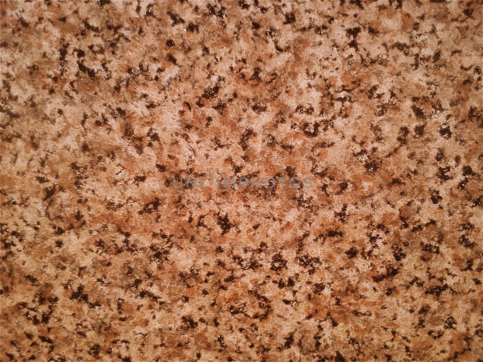 Granite smooth surface or slab in warm brown, gray, beige tones with frequent black spots and dots. Variant of interior decoration. Close-up. Natural background. Stone cut