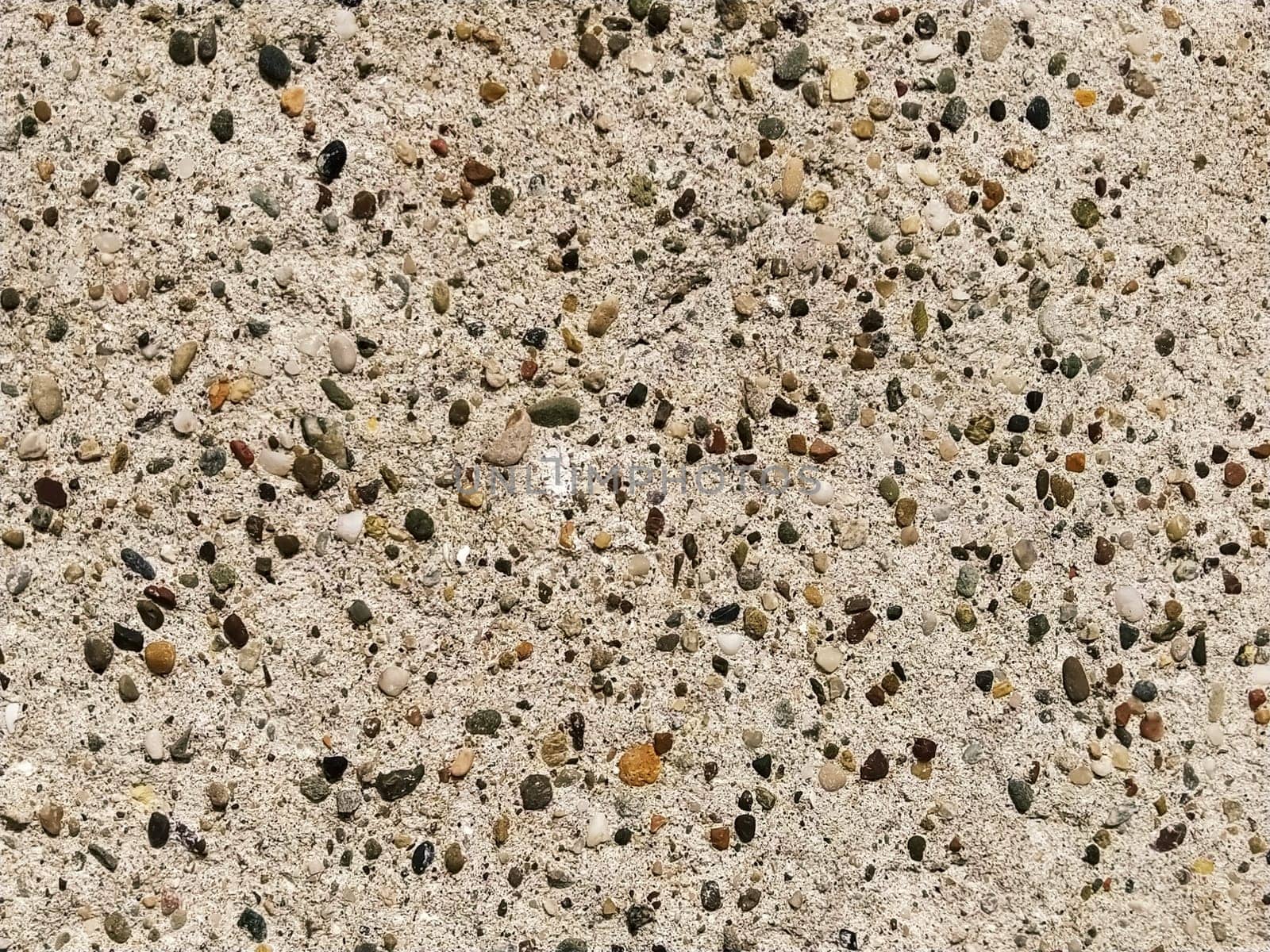 Concrete surface with multi-colored blotches of small stones. Light beige tone. Wall of a building or concrete slab. Close-up. Pockmarked cement surface. Interior or exterior finish option.