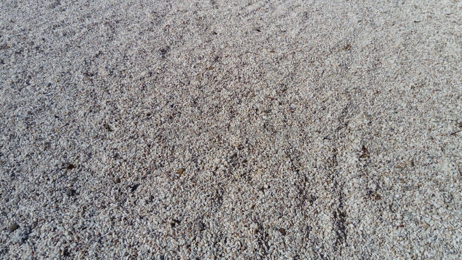 White small pebbles or decorative gravel. Natural daylight. The texture of the stone with a rough surface. Pebble beach.