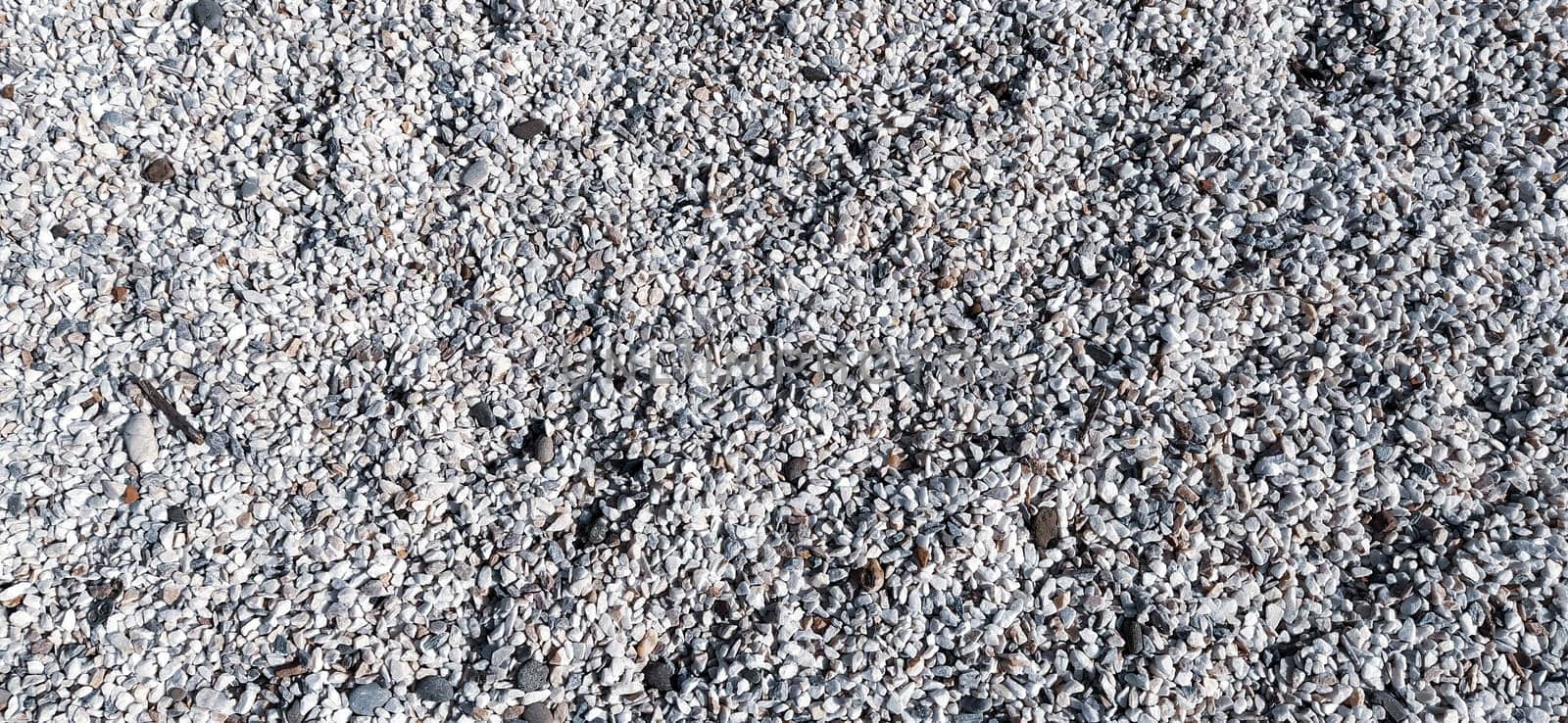 White small pebbles or decorative gravel. Natural daylight. The texture of the stone with a rough surface. Pebble beach.
