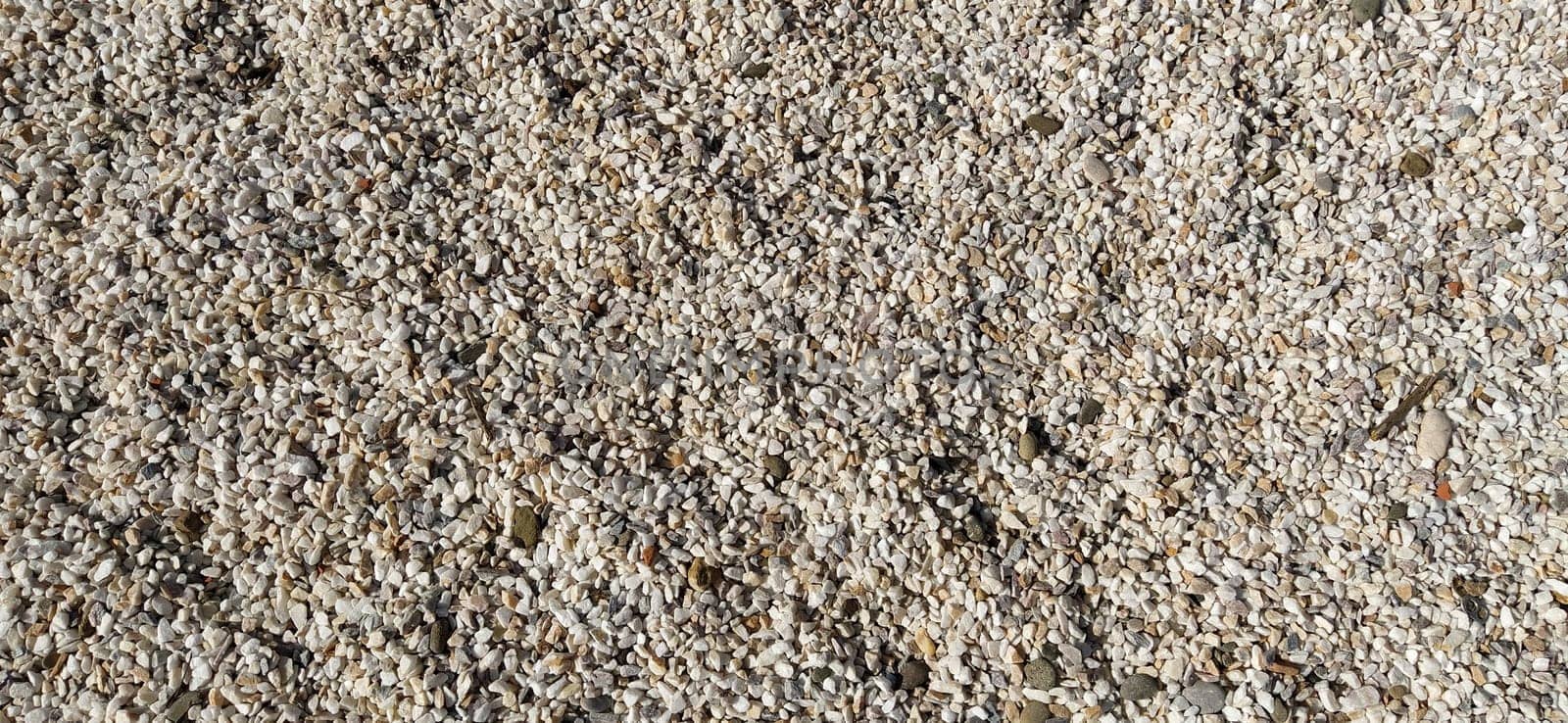 White small pebbles or decorative gravel. Natural daylight. The texture of the stone with a rough surface. Pebble beach.