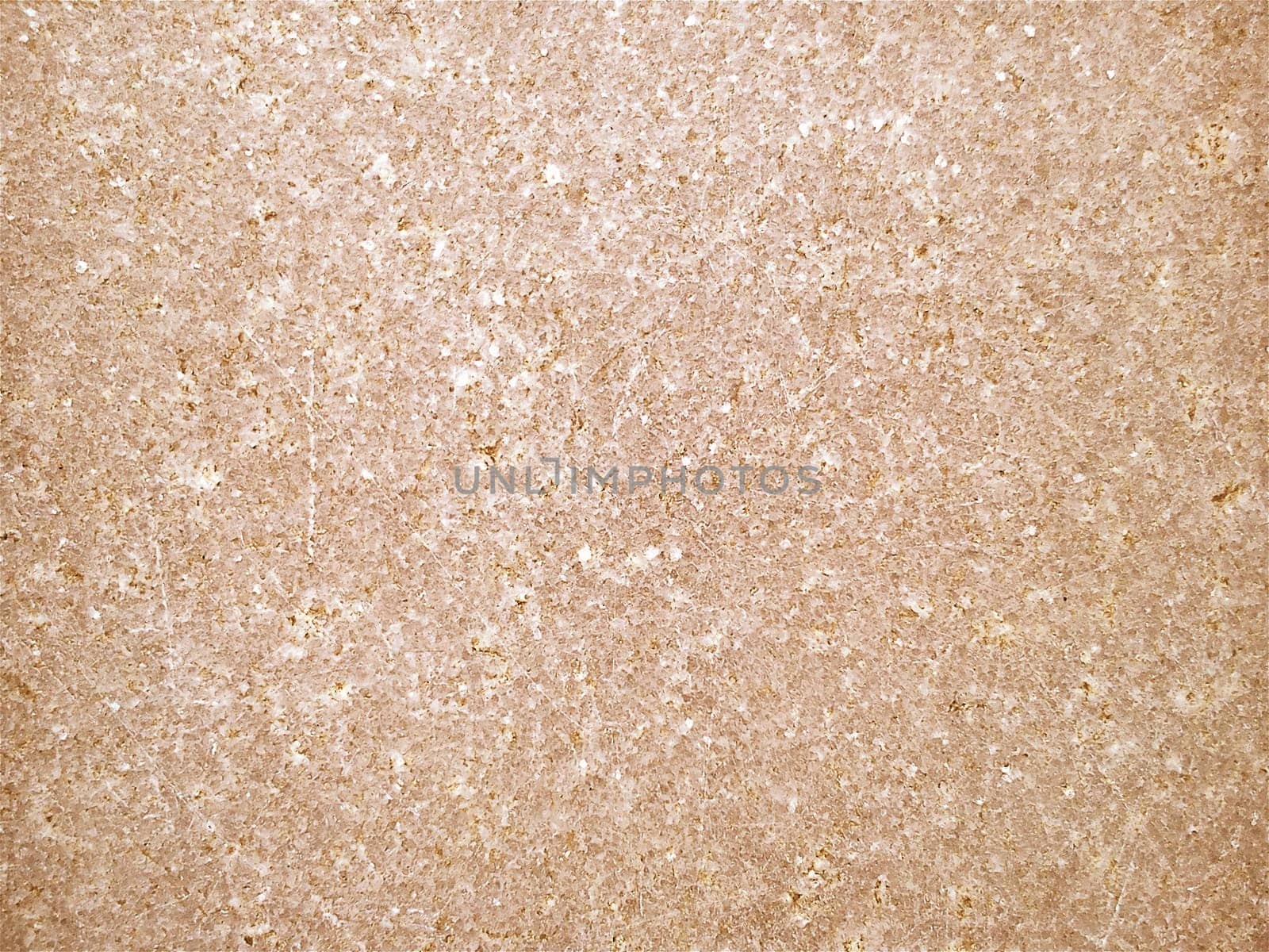 Granite is yellow-brown in color with small light and dark specks, uneven scratches. The texture of the stone. Warm colors and shades. Dim background.