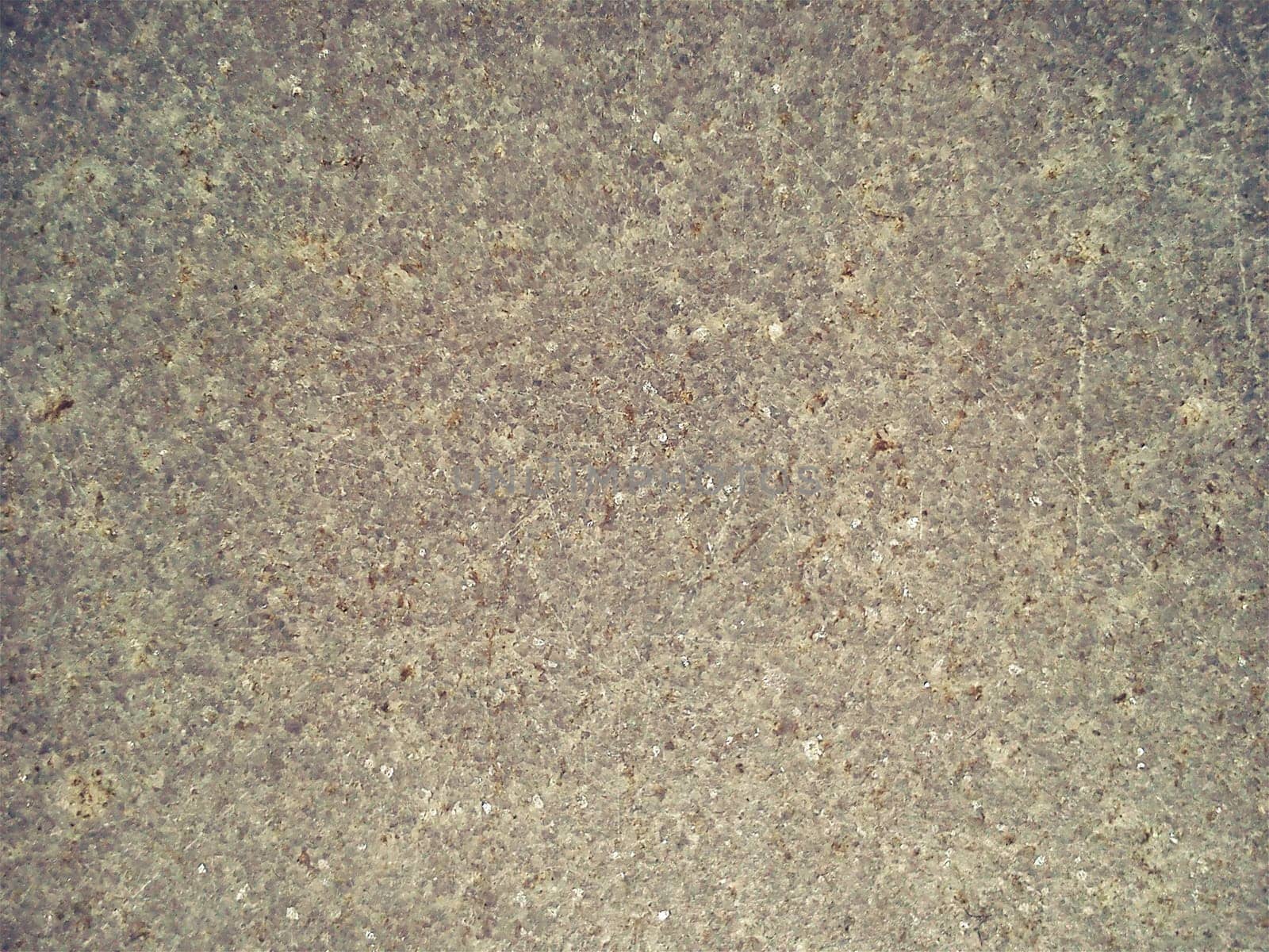 Granite is beige-brown in color with small light and dark specks, uneven scratches. The texture of the stone. Warm colors and shades. Dim background.