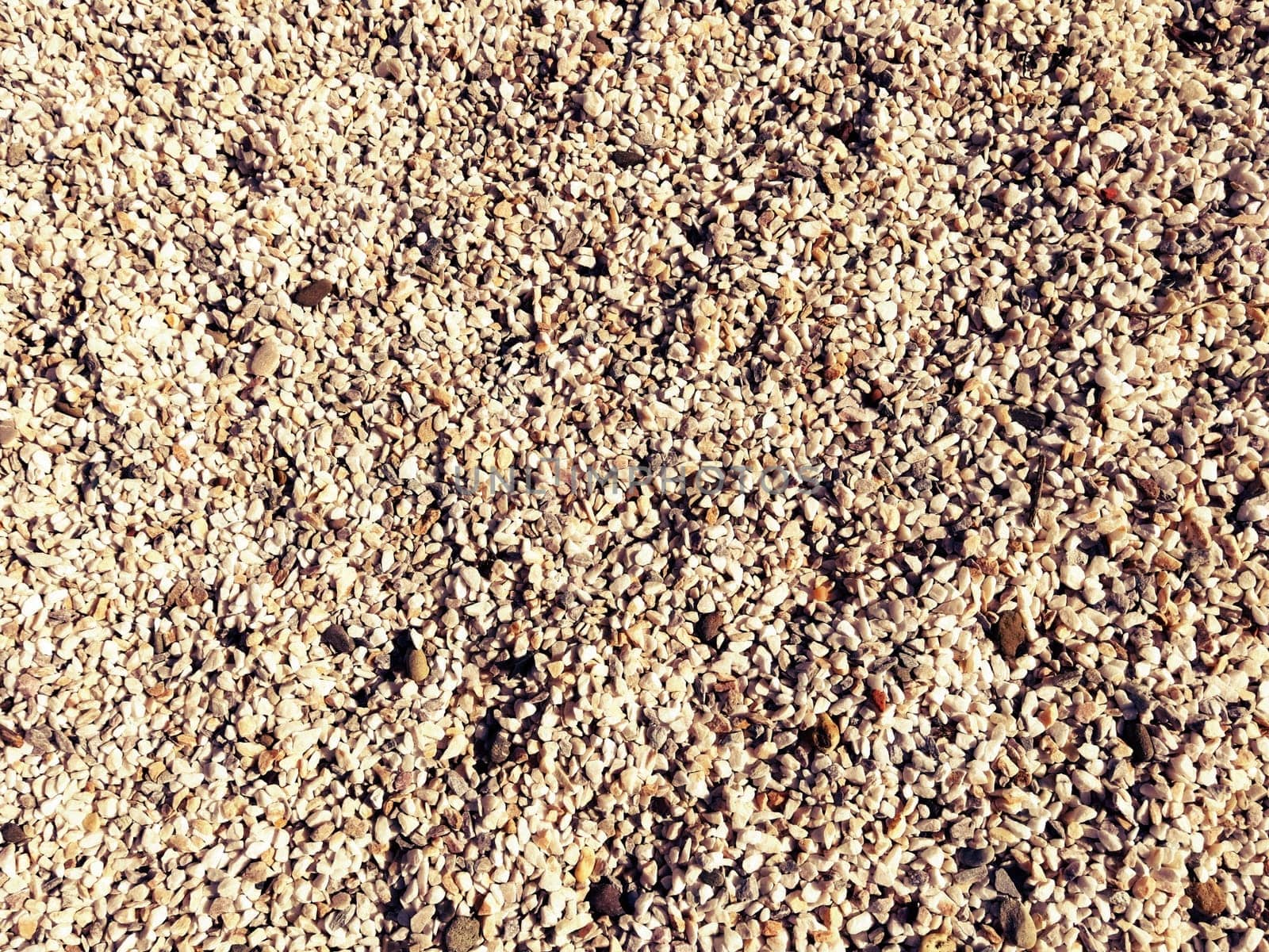 beige small pebbles or decorative gravel. Natural daylight. The texture of the stone with a rough surface. Pebble beach.