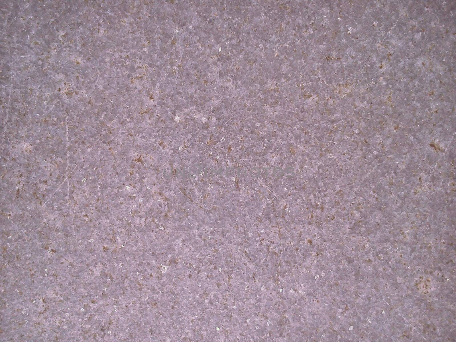 Granite of violet-pink color with small light and dark specks, uneven scratches. The texture of the stone. Warm colors and shades. Dim background.