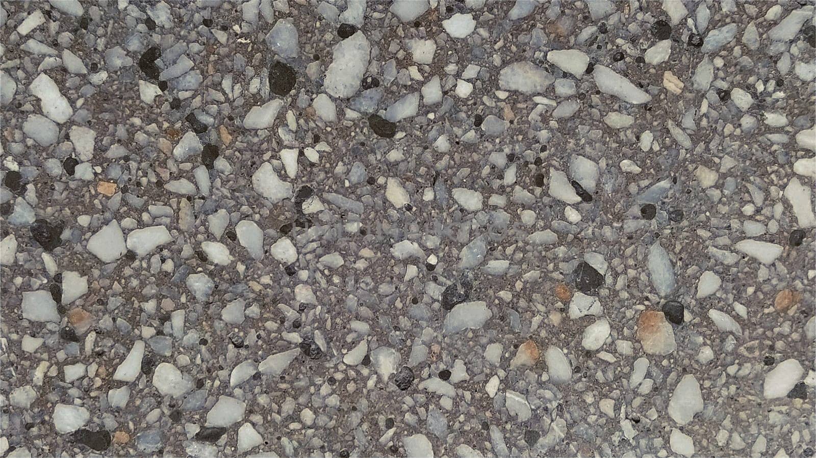Concrete surface with multi-colored spots of small stones. The gray wall of the building, concrete slab, or granite step. Close-up. Spotty cement surface. Interior or exterior decoration.