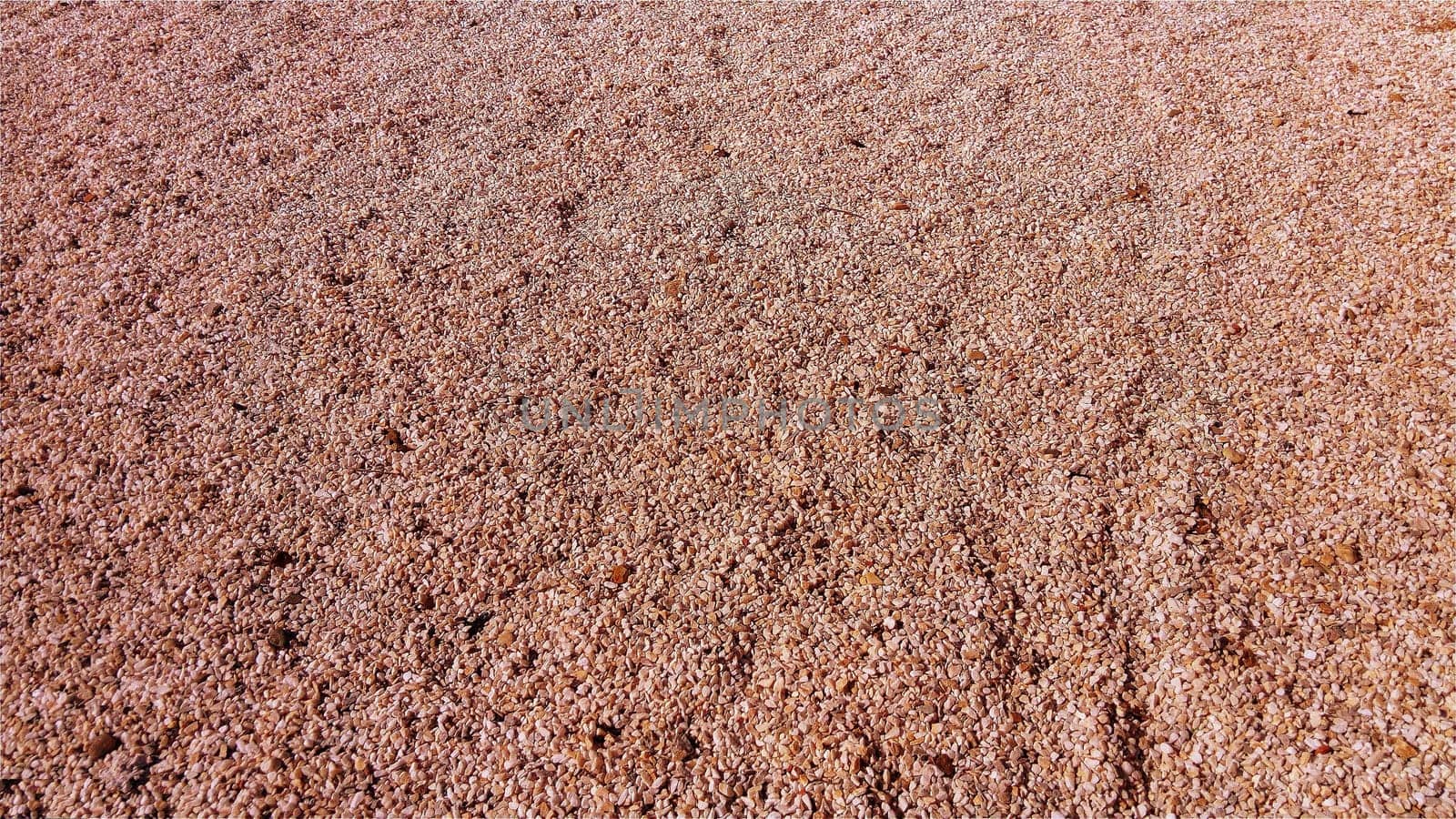 Red small pebbles or decorative gravel. Natural daylight. The texture of the stone with a rough surface. Pebble beach.