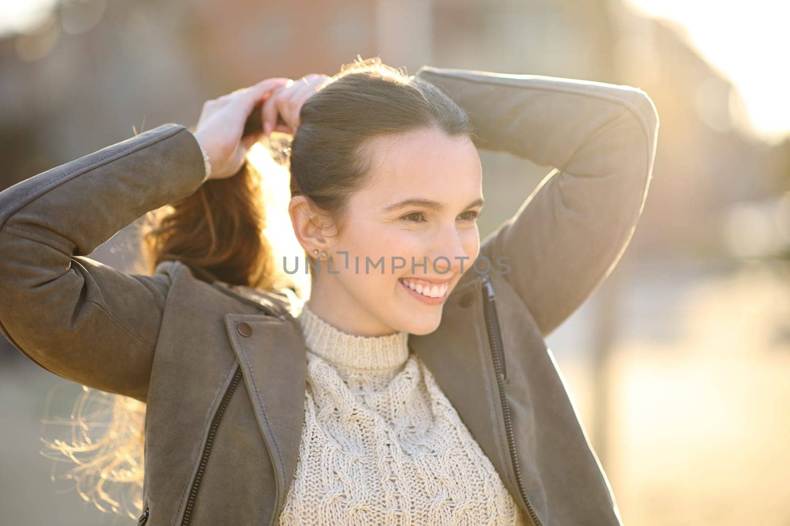 Happy woman making pony tail at sunset in the street