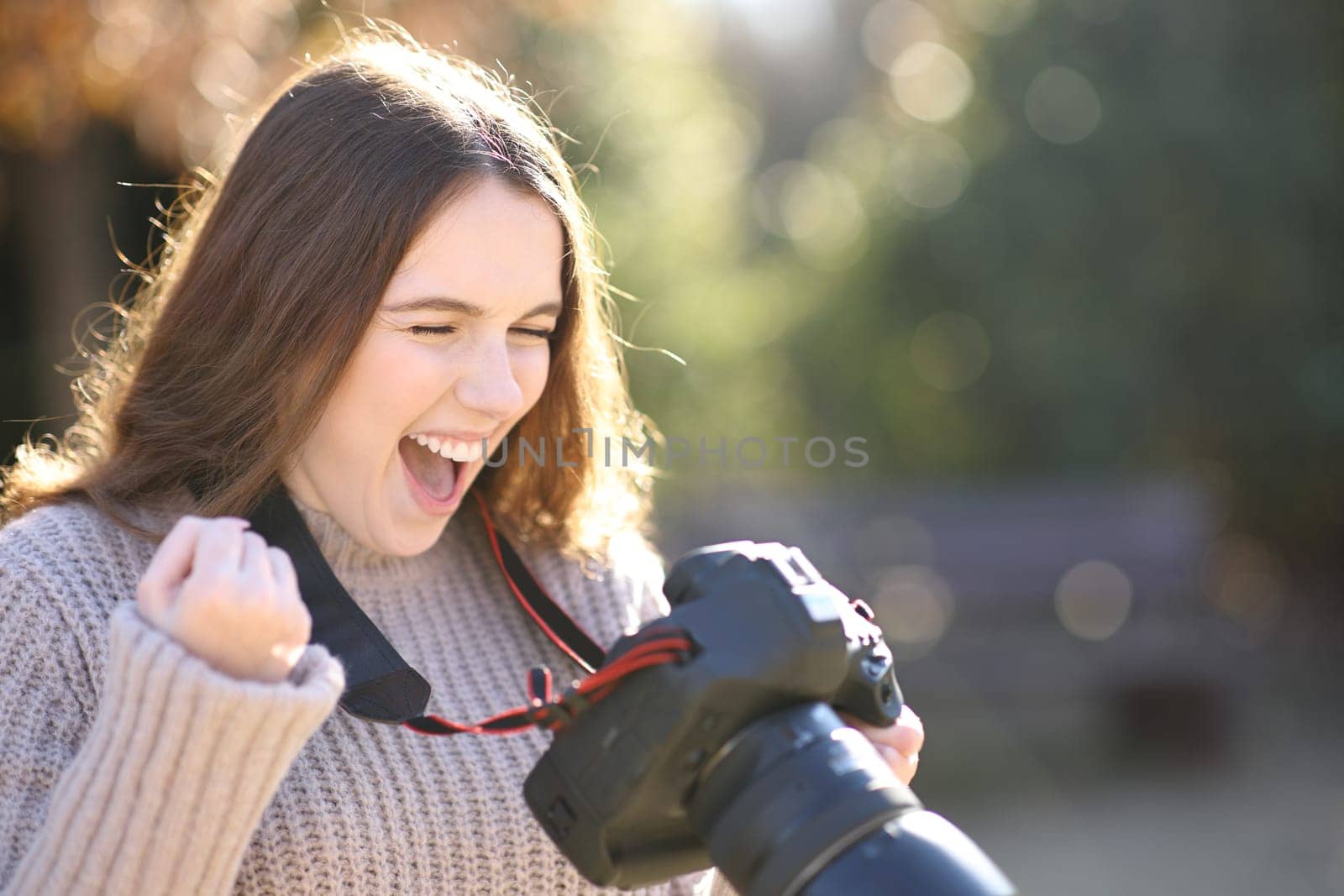 Excited photographer checking photos celebrating success on camera in winter