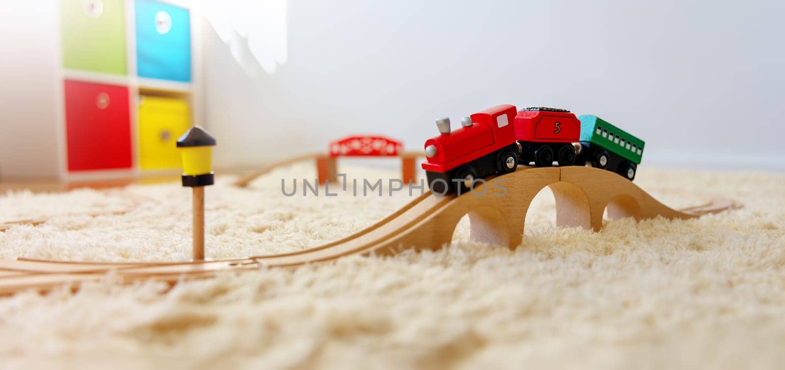 Closeup view of the toy train on the wooden bridge on the floor indoors. Panoramic background.