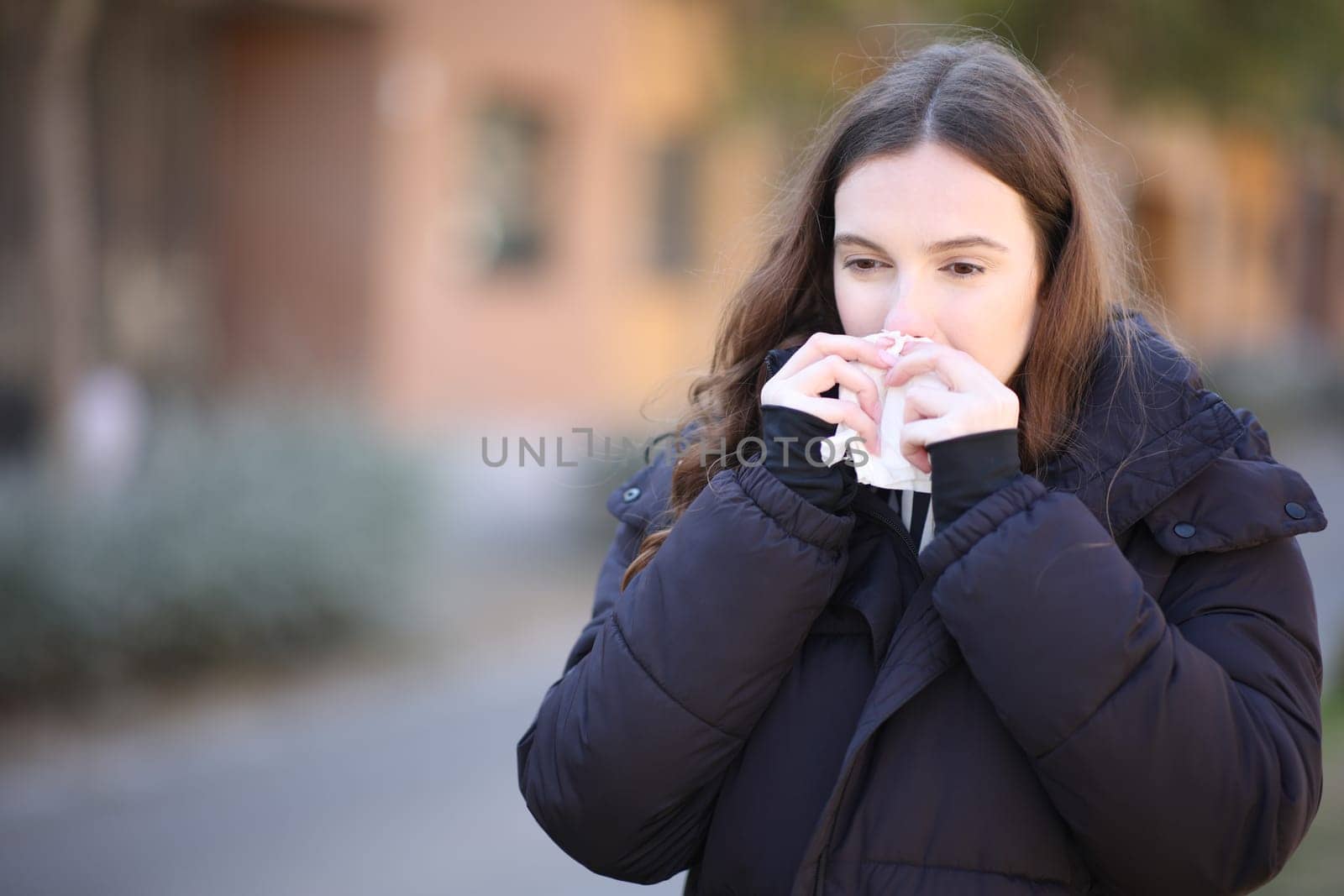 Ill woman using tissue to clean nose in the street in winter