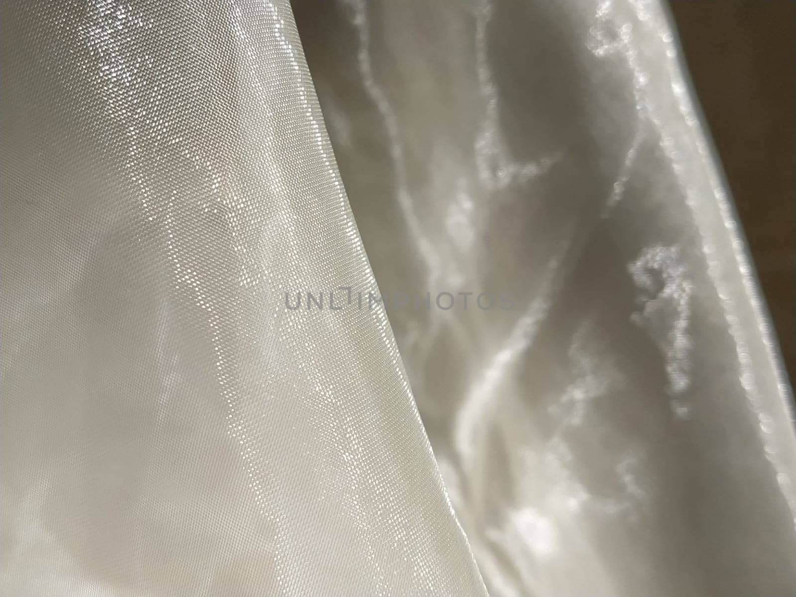 Organza in white and beige or champagne color close-up. Lightweight sheer tulle curtains under side lighting.