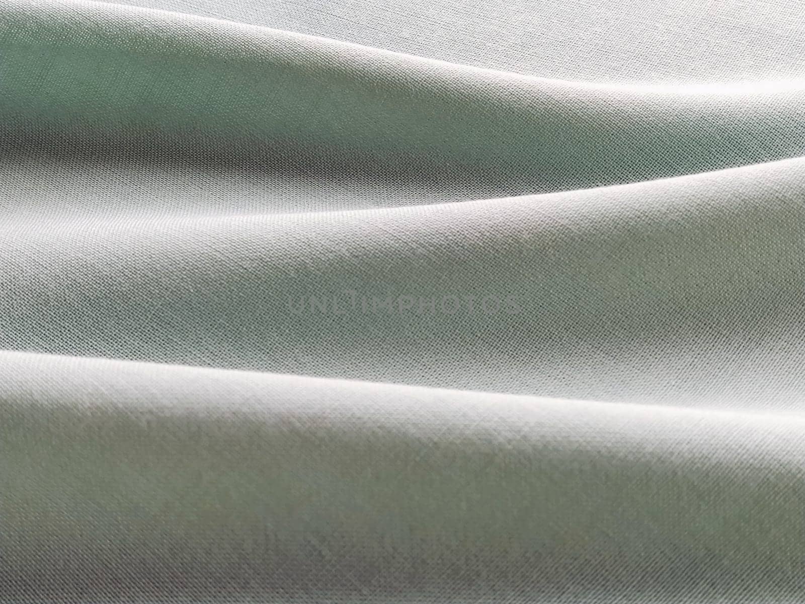 Beautifully folded light green fabric. Soft pleasant waves and flounces on textiles. Close-up. Drapery for curtains, fabric for dressmaking or upholstery.