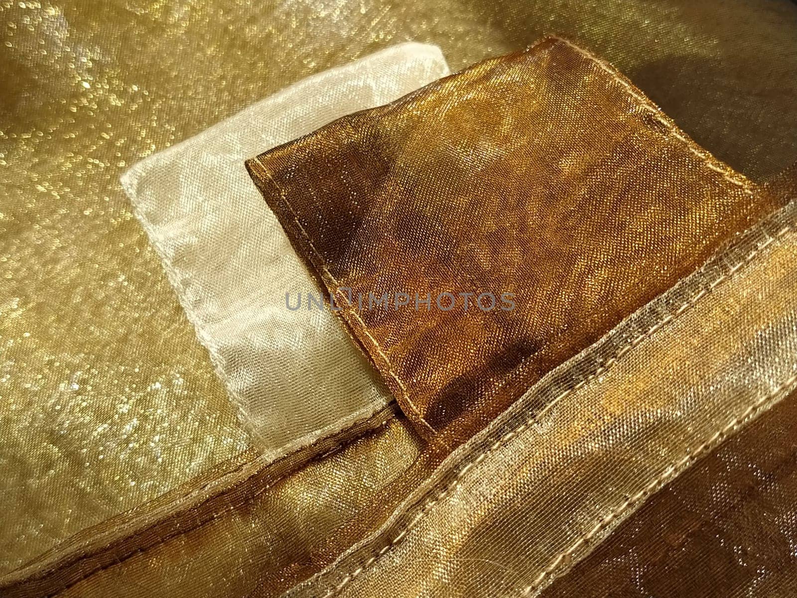 Curtain loops. Beautiful gold fabric. Organza in yellow, orange, beige and brown shades. Pleats in the fabric. Shiny gradient under the light. Folded silky tulle. Transparent curtain material.