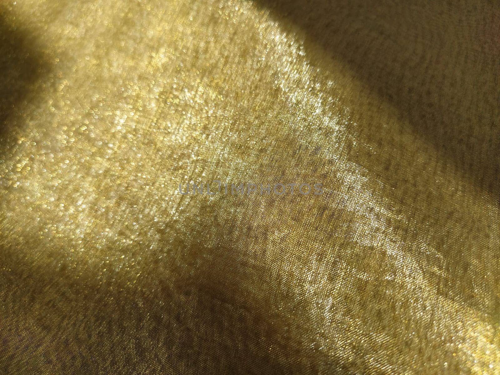 Beautiful gold fabric. Organza in yellow, orange, beige and brown shades. Pleats in the fabric. Shiny gradient under the light. Folded silky tulle. Transparent curtain material.