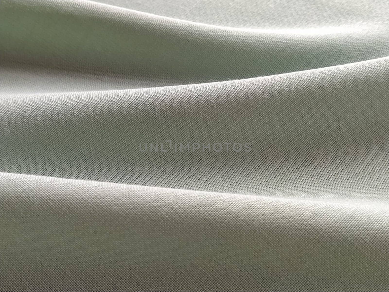 Beautifully folded light green fabric. Soft pleasant waves and flounces on textiles. Close-up. Drapery for curtains, fabric for dressmaking or upholstery.