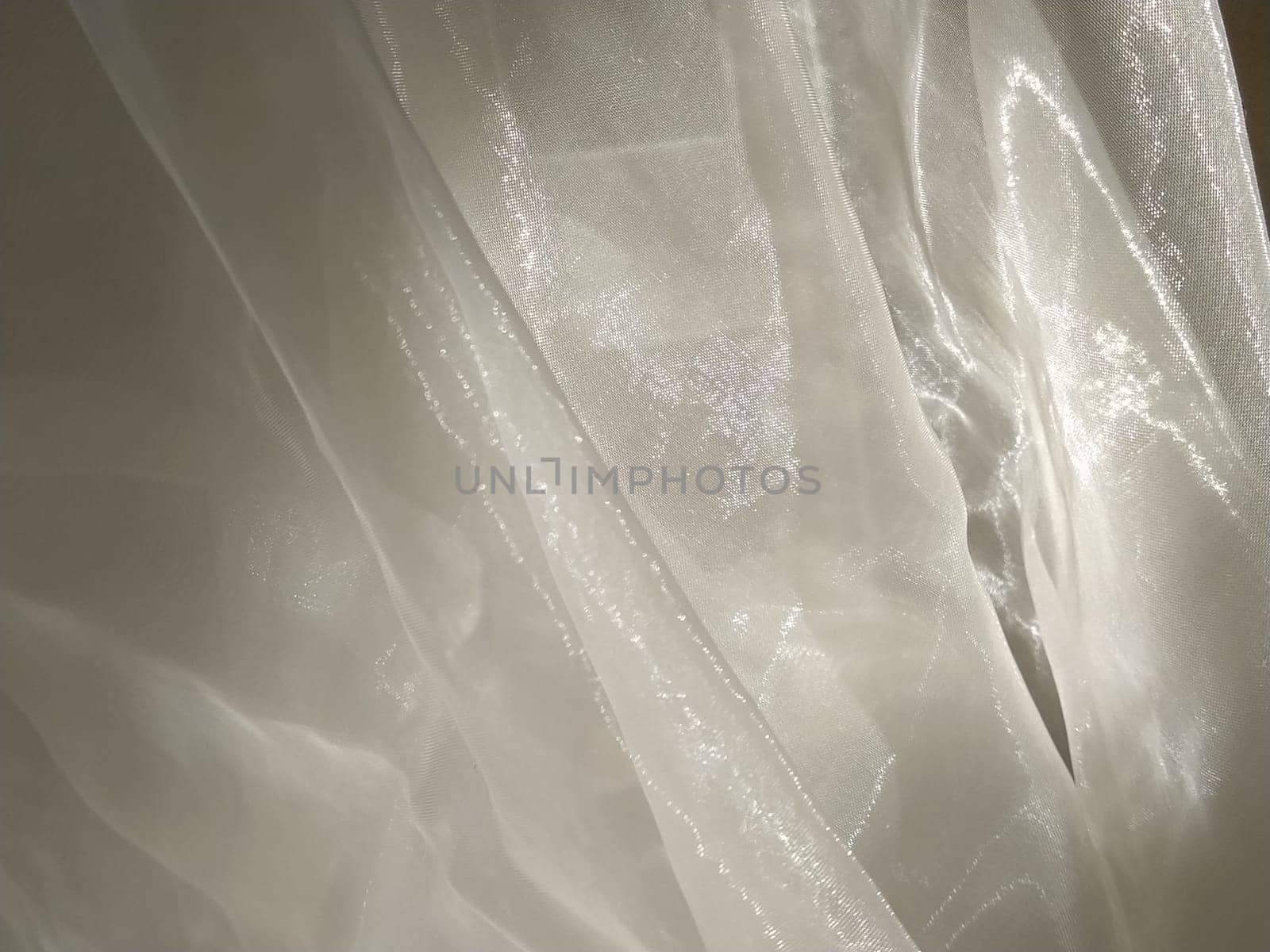 Organza in white and beige or champagne color close-up. Lightweight sheer tulle curtains under side lighting.