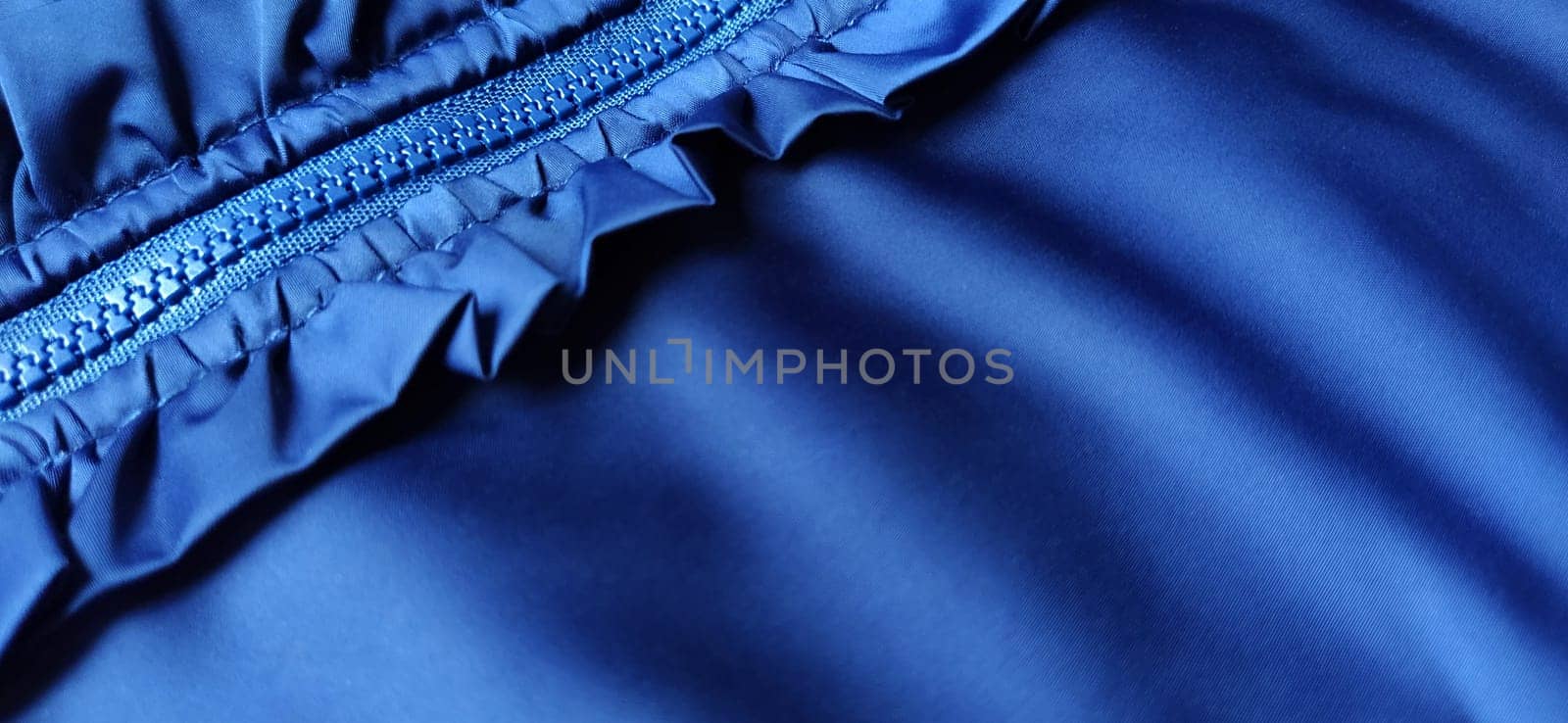 Buttoned zip on a blue raincoat. Waves and folds in the fabric. Beautiful flounces, ruffles, frills. Decorative finishing of a garment. Smocked, sewn silk fabric. Nice casual wear