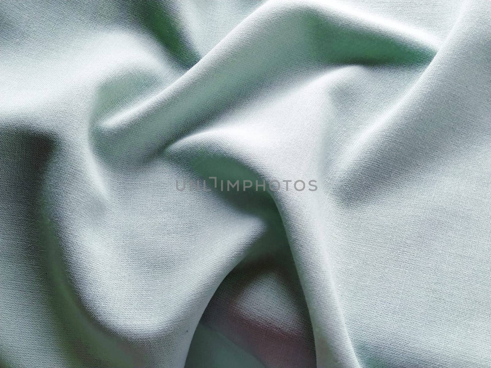 Beautifully folded light green fabric. Soft pleasant waves and flounces on textiles. Close-up. Drapery for curtains, fabric for dressmaking or upholstery.